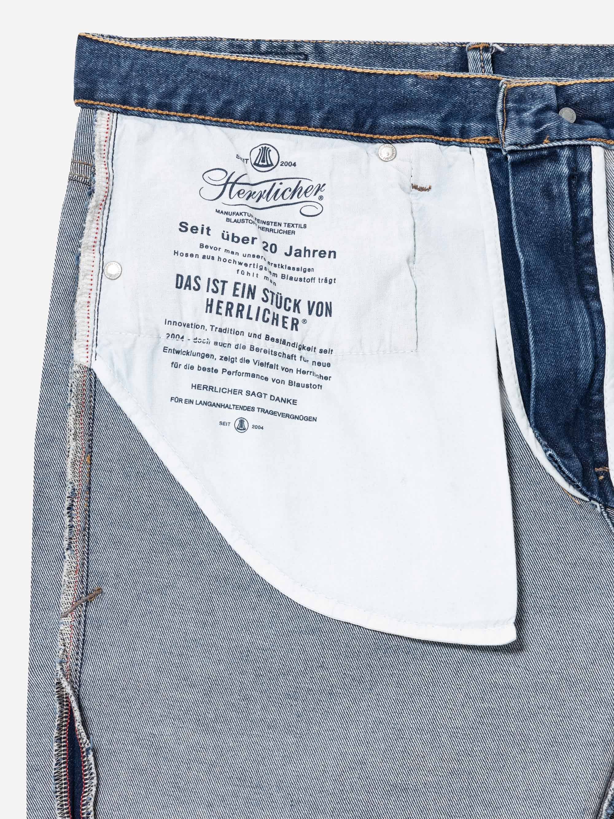 Nahaufnahme der Innenseite einer blauen Jeans, die das weiße Taschenfutter mit schwarzem, aufgedrucktem deutschen Text und die Nähte auf dem Jeansstoff zeigt.