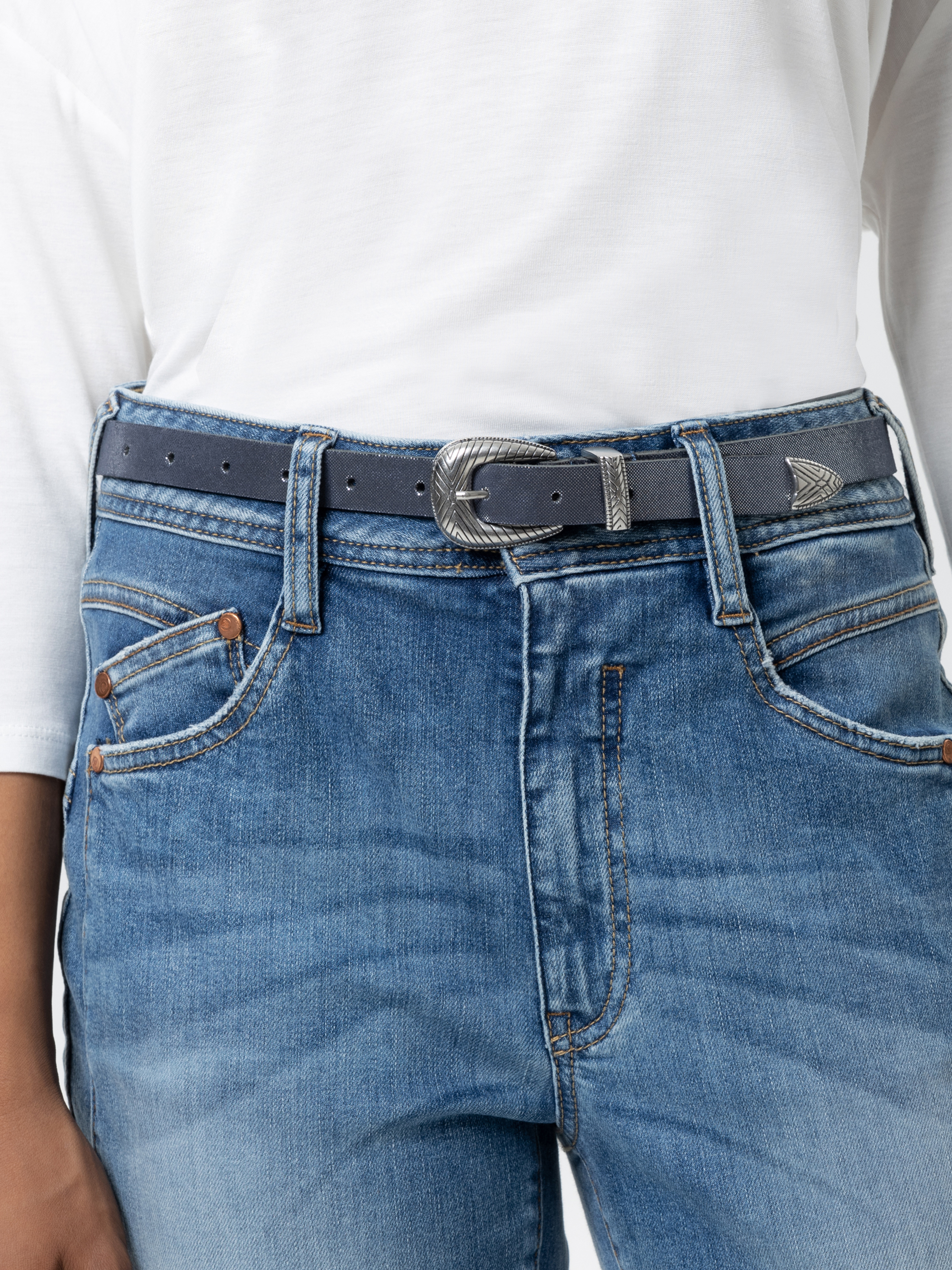Eine Person, die ein weißes Hemd trägt, das in eine blaue Jeans gesteckt wird, und einen blauen Gürtel mit einer silbernen Schnalle und einer Zierspitze.