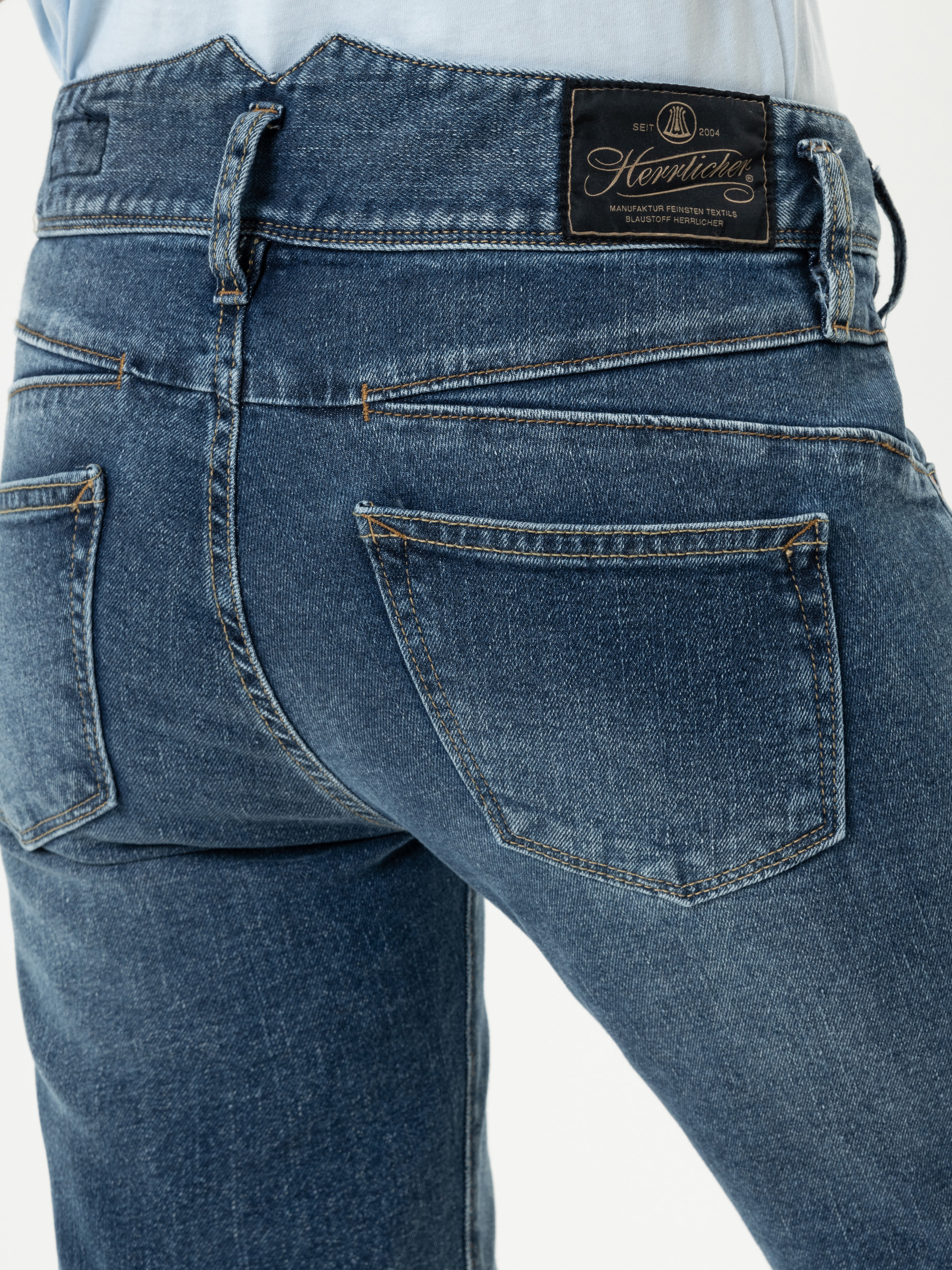 Nahaufnahme einer Person, die eine blaue Denim-Jeans trägt, von hinten gesehen, mit zwei Gesäßtaschen und einem schwarzen Markenetikett aus Leder am Bund.