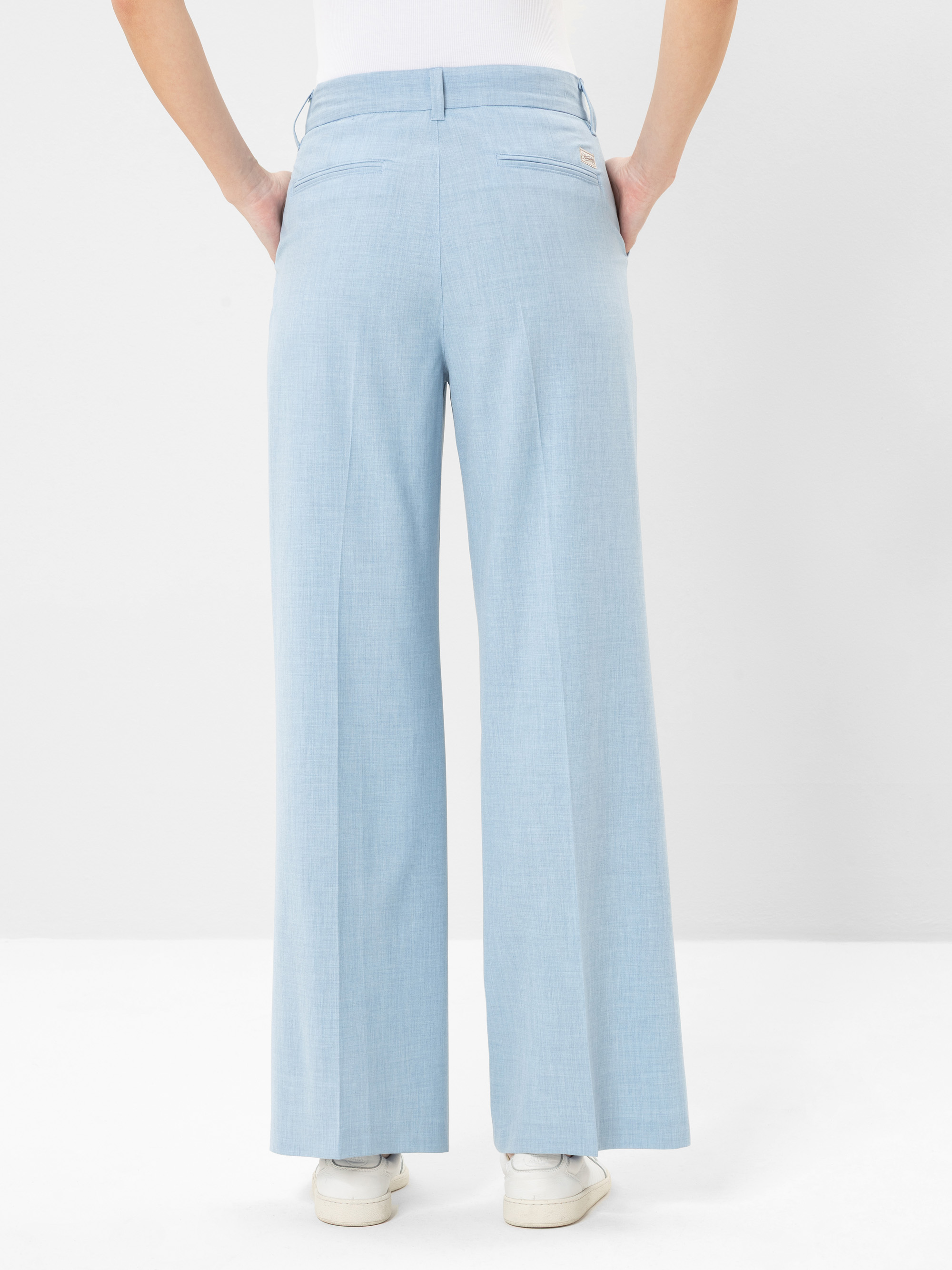 Eine Person, die eine hellblaue Hose mit weitem Bein und weiße Turnschuhe trägt, steht mit dem Gesicht nach hinten, die Hände in den Gesäßtaschen, vor einem schlichten weißen Hintergrund.