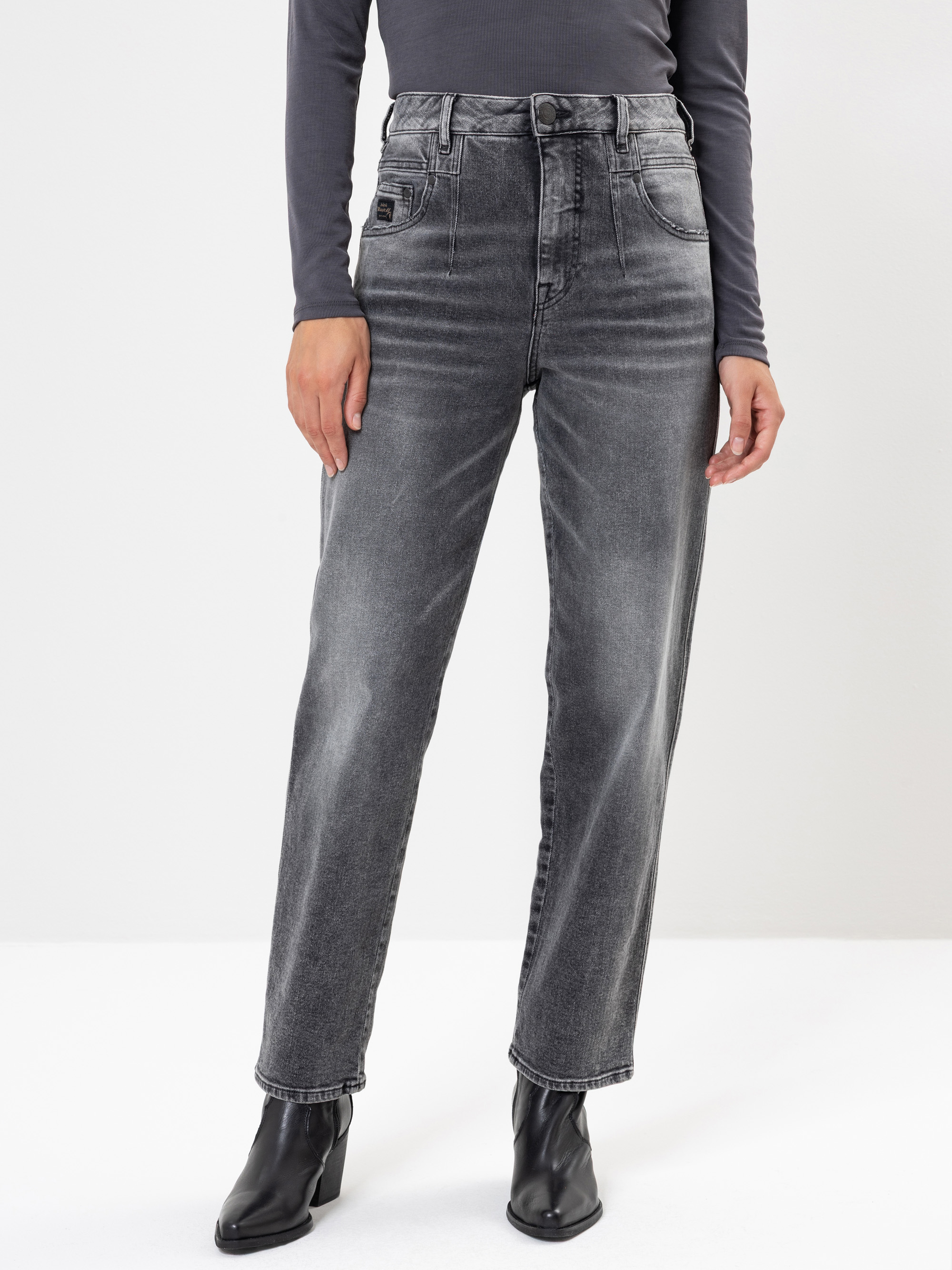 Eine Person, die eine verblichene schwarze Jeans mit hoher Taille und geradem Bein, ein langärmeliges dunkelgraues Oberteil und schwarze Stiefeletten trägt, steht vor einem schlichten weißen Hintergrund. Ihr Gesicht ist nicht zu sehen.