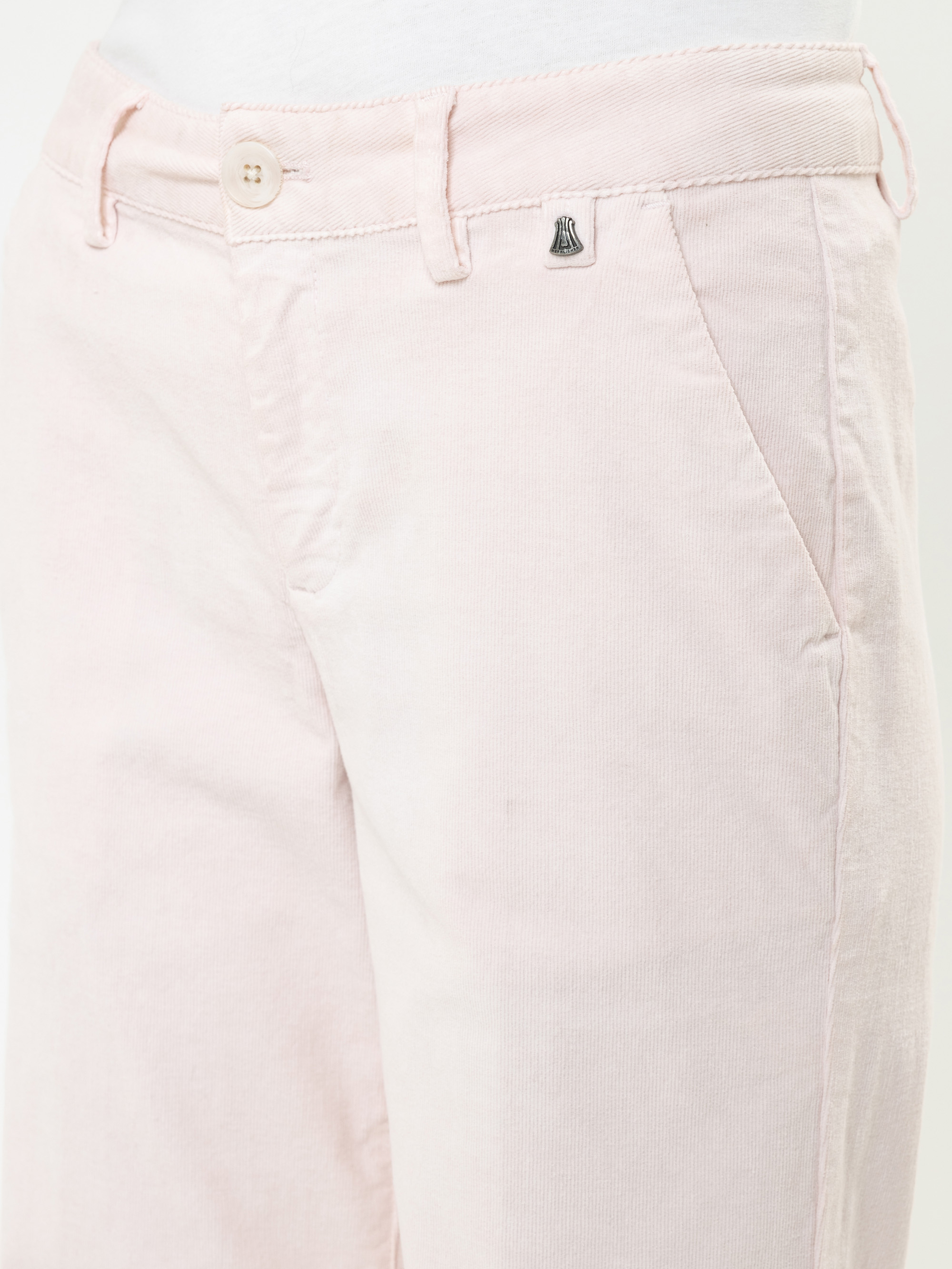 Nahaufnahme einer Person, die eine hellrosa Hose mit Seitentaschen, einem Knopf und einem Reißverschluss sowie einem kleinen Metallemblem in der Nähe des Hosenbundes trägt.