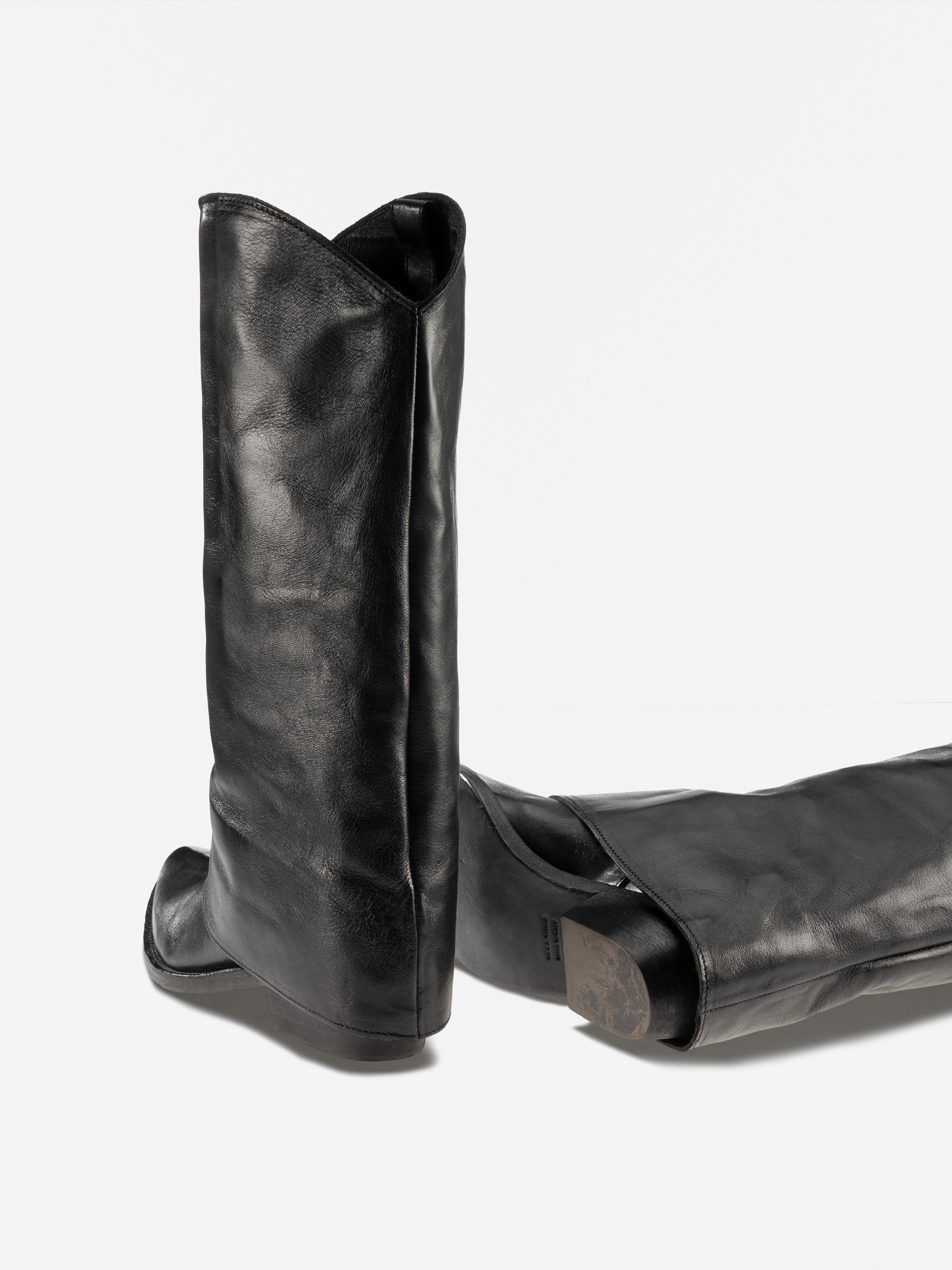 Zwei schwarze Cowboystiefel aus Leder sind auf einem schlichten weißen Hintergrund abgebildet, wobei ein Stiefel aufrecht steht und der andere auf der Seite liegt. Die Stiefel haben ein einfaches, schnörkelloses Design mit einer leicht spitzen Schuhspit