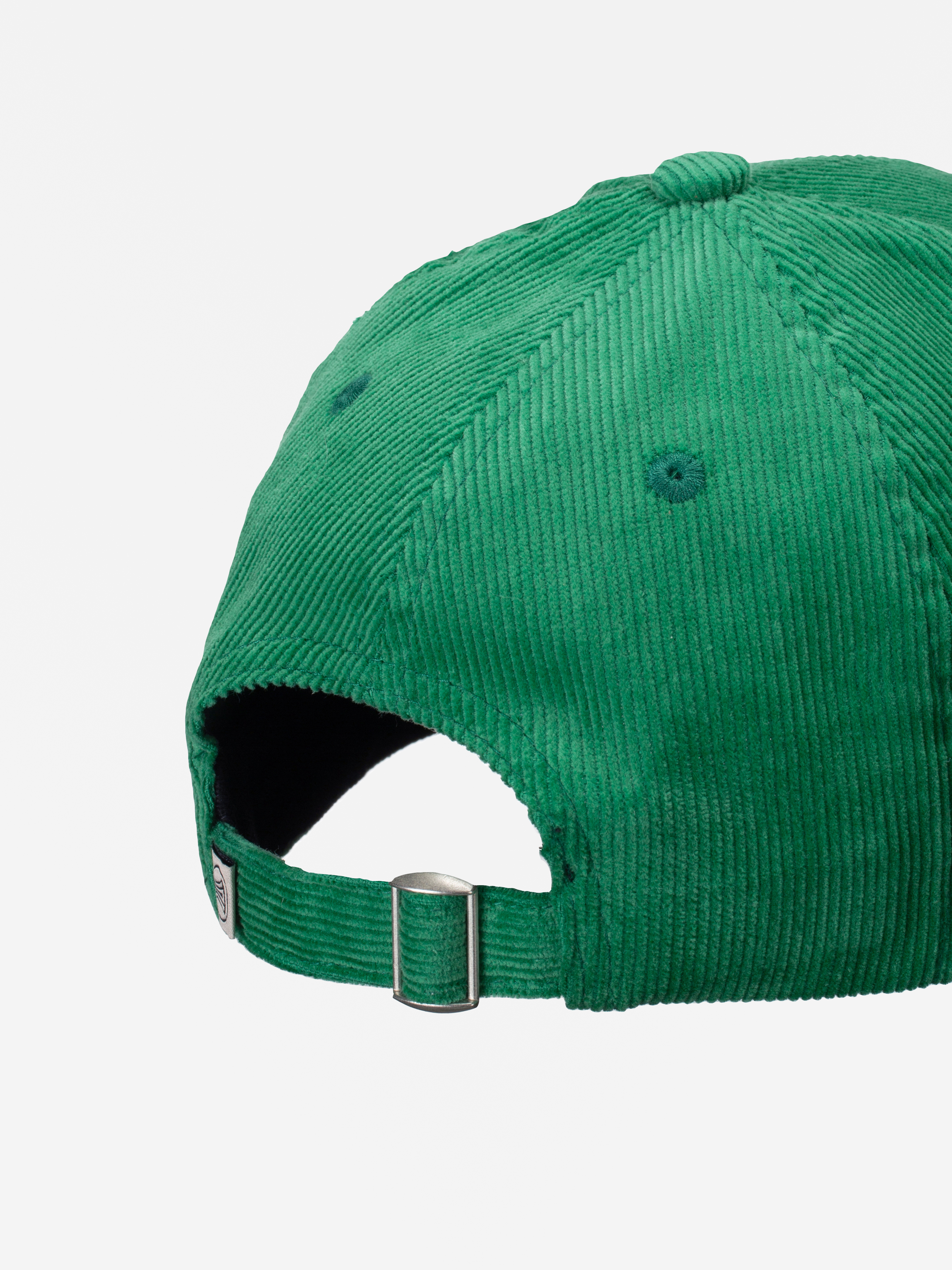 Nahaufnahme der Rückseite einer Baseballmütze aus grünem Cord mit aufgenähten Ösen und einem verstellbaren Riemen mit Metallschließe. Der Hintergrund ist einfarbig weiß.