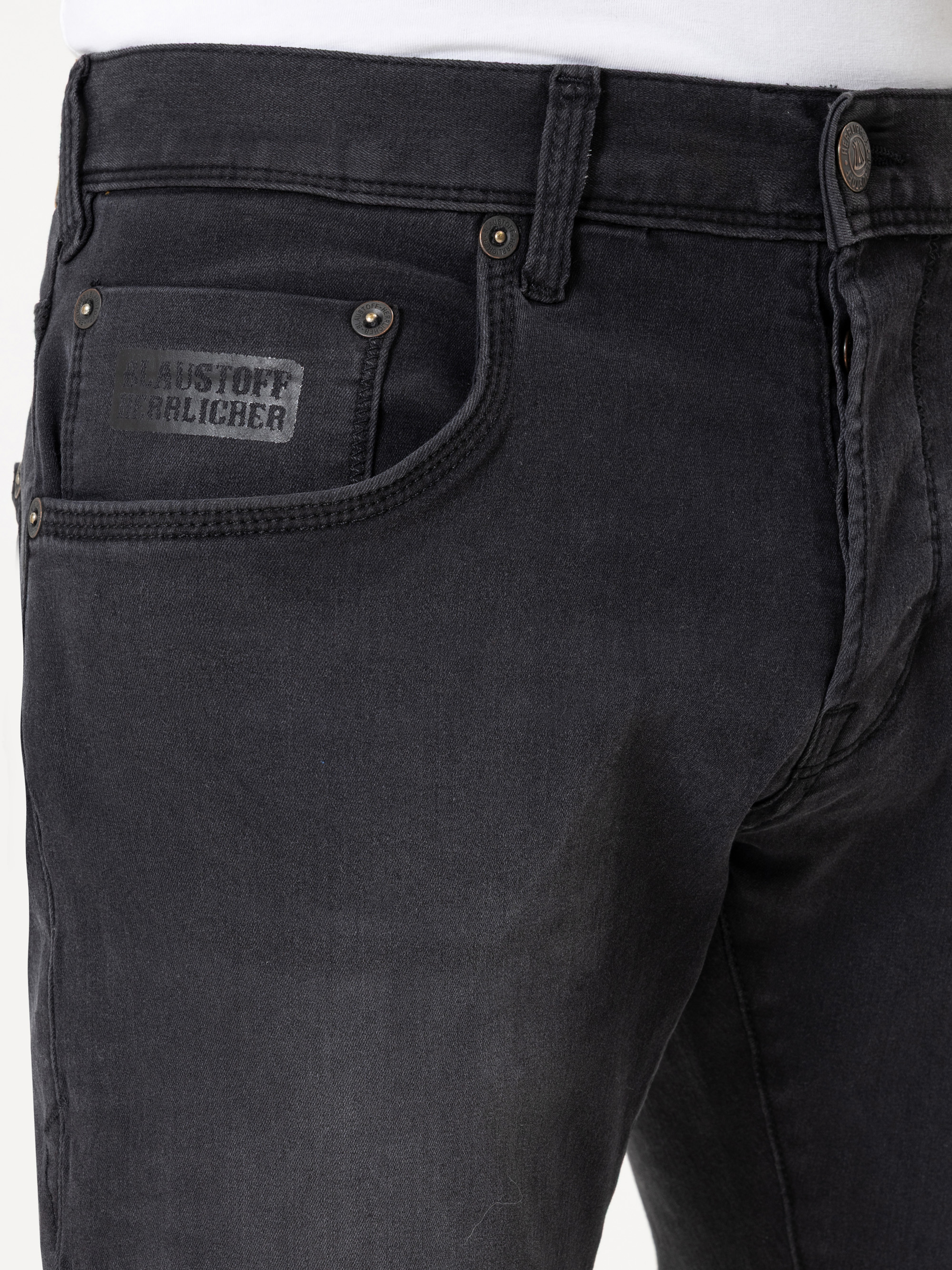 Nahaufnahme einer Person, die eine schwarze Jeans mit einer sichtbaren Vordertasche und einem kleinen schwarzen Etikett mit der Aufschrift RAUSTOFF BALICHER trägt. Die Person trägt außerdem ein weißes Oberteil.