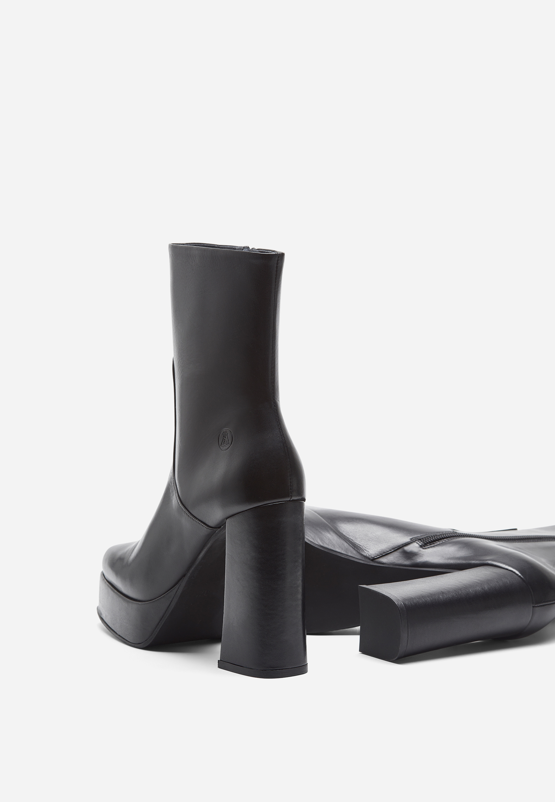 Schwarze Plateau-Stiefel mit Blockabsätzen, dargestellt auf weißem Hintergrund. Ein Stiefel steht aufrecht und zeigt einen seitlichen Reißverschluss und eine abgerundete Schuhspitze, während der andere Stiefel auf der Seite liegt und die Sohle offenba