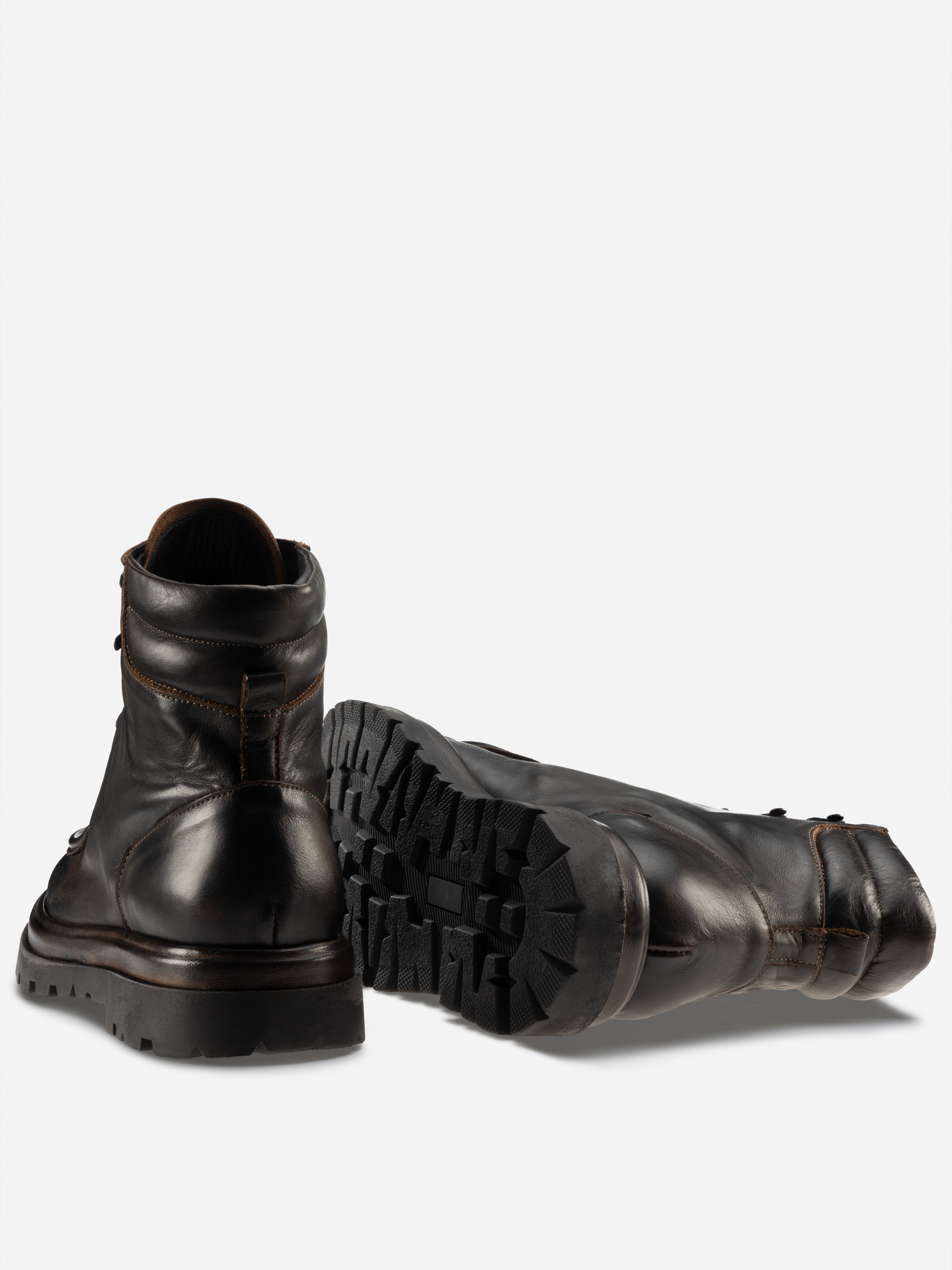 Ein Paar robuster schwarzer Lederstiefel; ein Stiefel steht aufrecht und zeigt die Rückseite und den Absatz, während der andere auf der Seite liegt und die dicke, strukturierte Sohle zeigt.