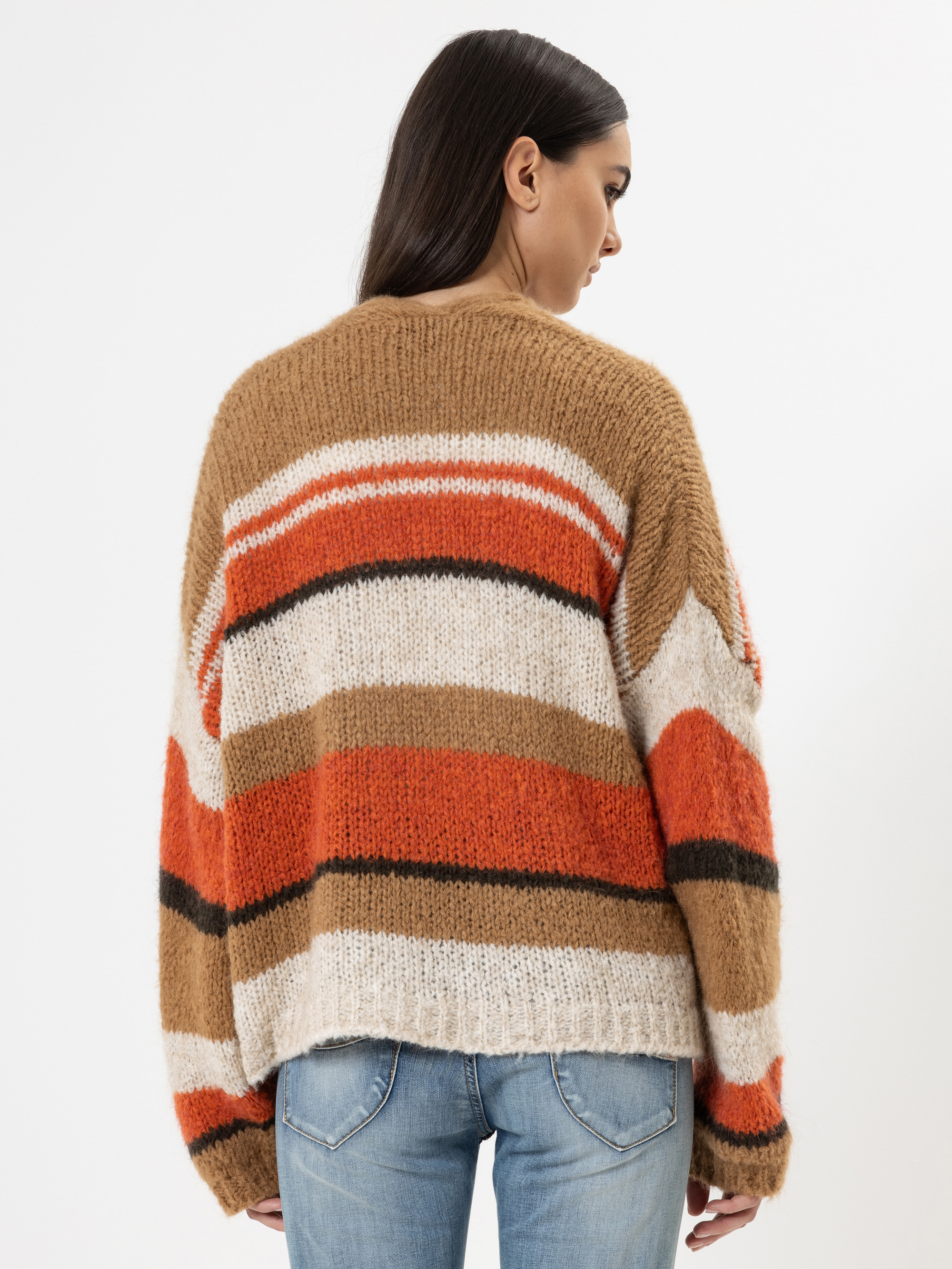 Eine Frau mit langen dunklen Haaren, von hinten gesehen, trägt einen gemütlichen, übergroßen Pullover mit horizontalen Streifen in Orange, Braun, Schwarz und Weiß, gepaart mit hellblauen Jeans vor einem schlichten weißen Hintergrund.