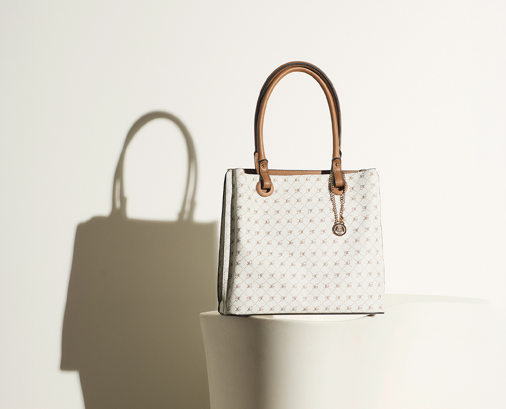 Eine elegante weiße Handtasche mit hellbraunen Griffen und einem dezenten geometrischen Muster sitzt auf einer weißen Fläche und wirft einen deutlichen Schatten auf den weißen Hintergrund.