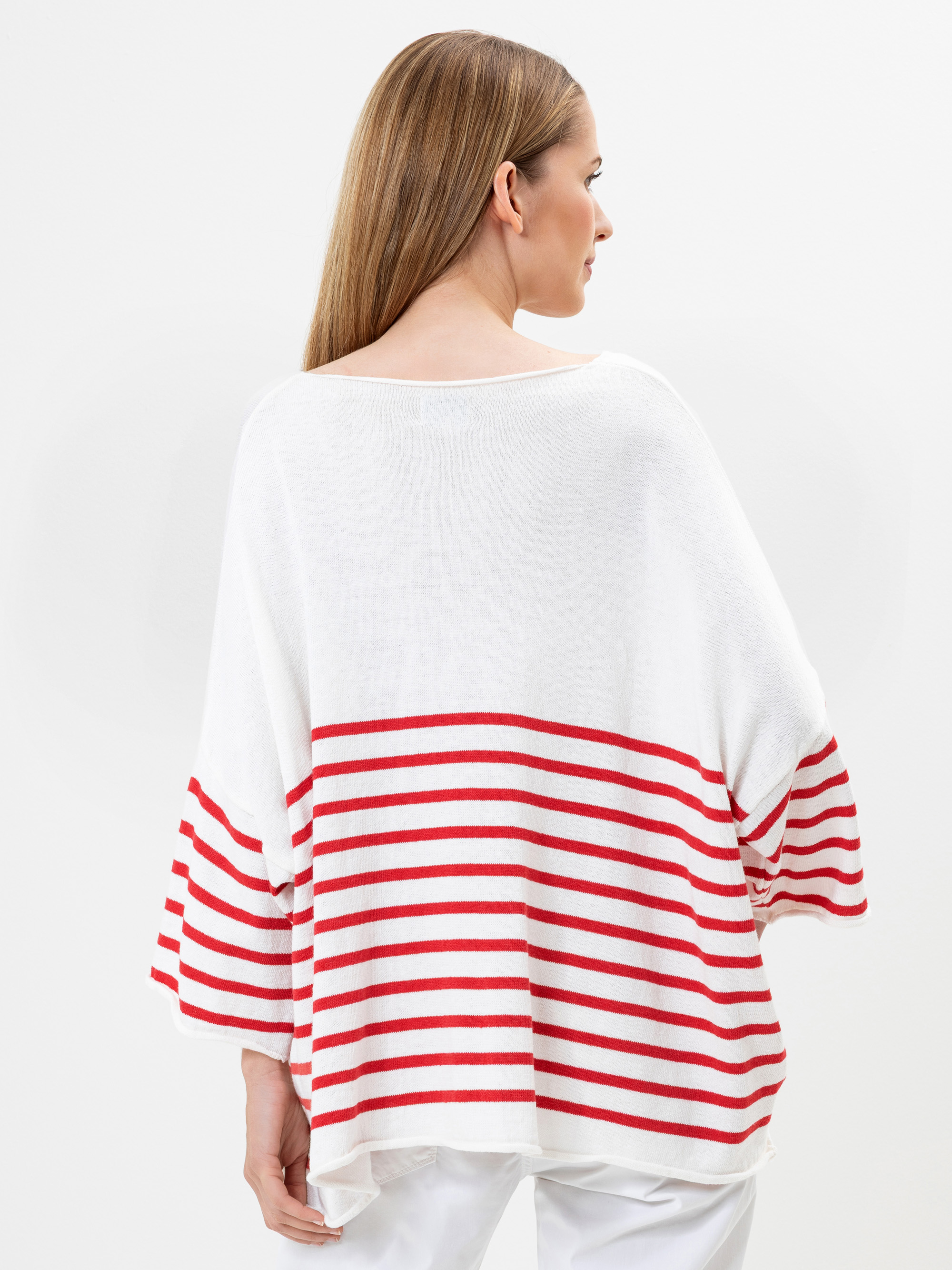 Eine Frau mit langem glattem Haar, von hinten gesehen, trägt ein lockeres weißes Oberteil mit roten Querstreifen in der unteren Hälfte und an den Ärmeln, gepaart mit einer weißen Hose. Der Hintergrund ist einfarbig weiß.