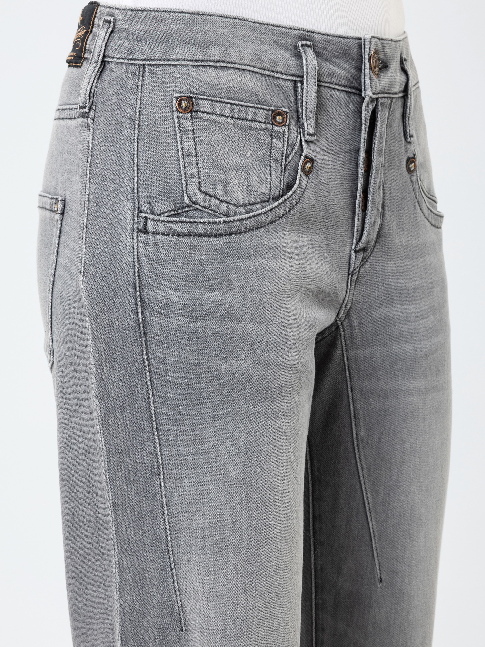 Nahaufnahme einer Person, die eine hellgraue Jeans mit hoher Taille, Vordertaschen und sichtbaren Nähten trägt, von der Taille bis zur Mitte des Oberschenkels vor einem unifarbenen Hintergrund.