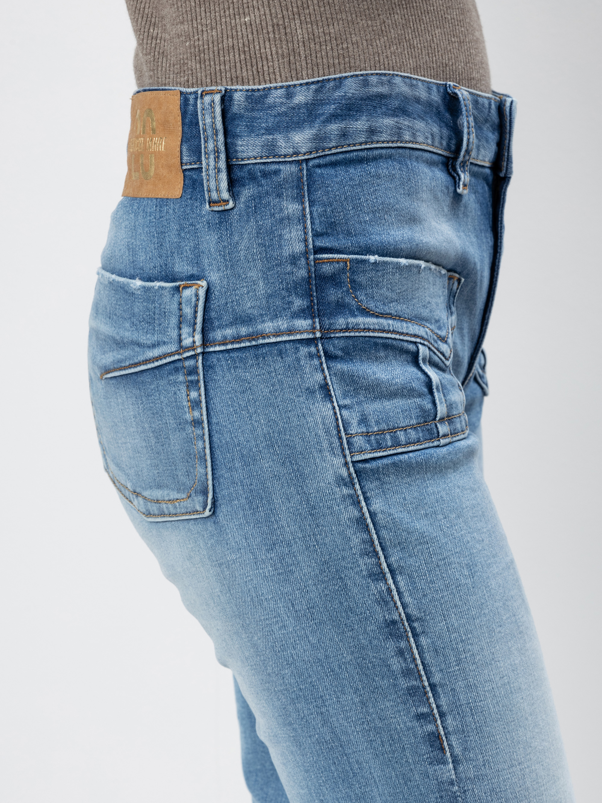 Person, die eine hellblaue Jeans und ein graues geripptes Oberteil trägt, von der Seite gesehen. Die Jeans hat sichtbare Nähte, einen Lederaufnäher am Bund und einen verblichenen, abgenutzten Look.