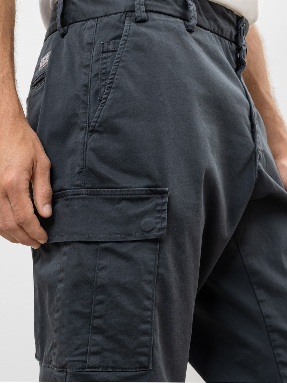 Nahaufnahme einer Person, die eine dunkelgraue Cargoshorts trägt, wobei der Schwerpunkt auf der Seitentasche und dem Bundbereich liegt und die Hand der Person in der Nähe der Cargotasche ruht.