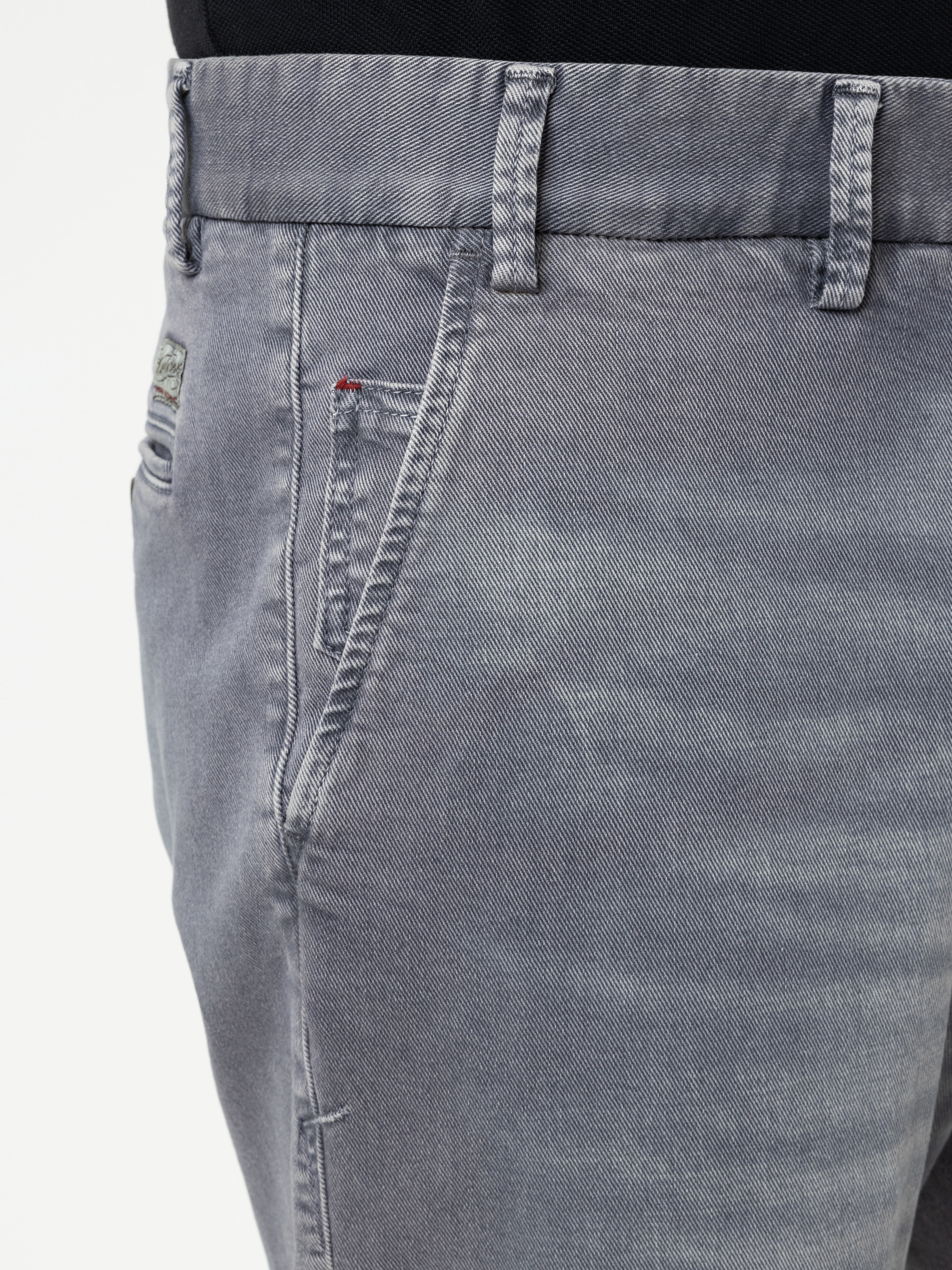 Nahaufnahme einer Person, die eine hellgraue Jeans mit sichtbarer Vordertasche und Gürtelschlaufen sowie ein schwarzes Hemd trägt, das teilweise in der Taille gesteckt ist.