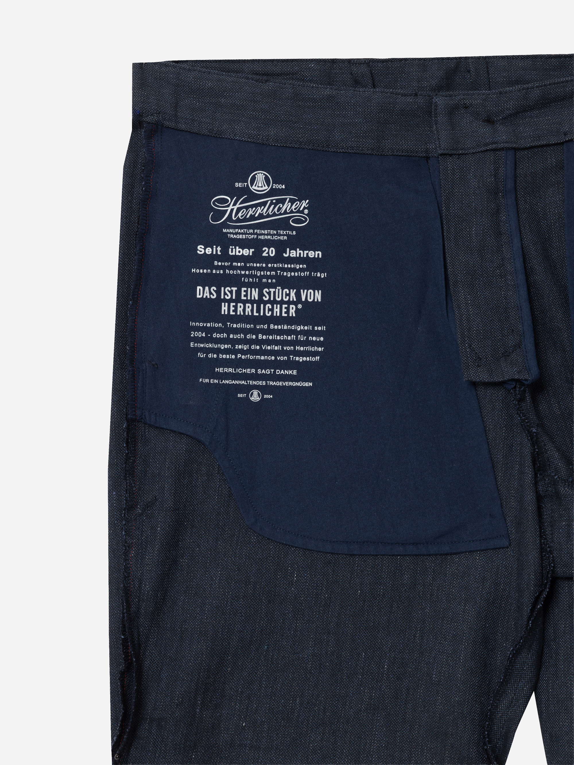 Nahaufnahme der Innenseite einer dunklen Denim-Jeans, die ein marineblaues Taschenfutter mit weißem deutschem Text, Markenzeichen und Produktinformationen auf dem Stoff zeigt.