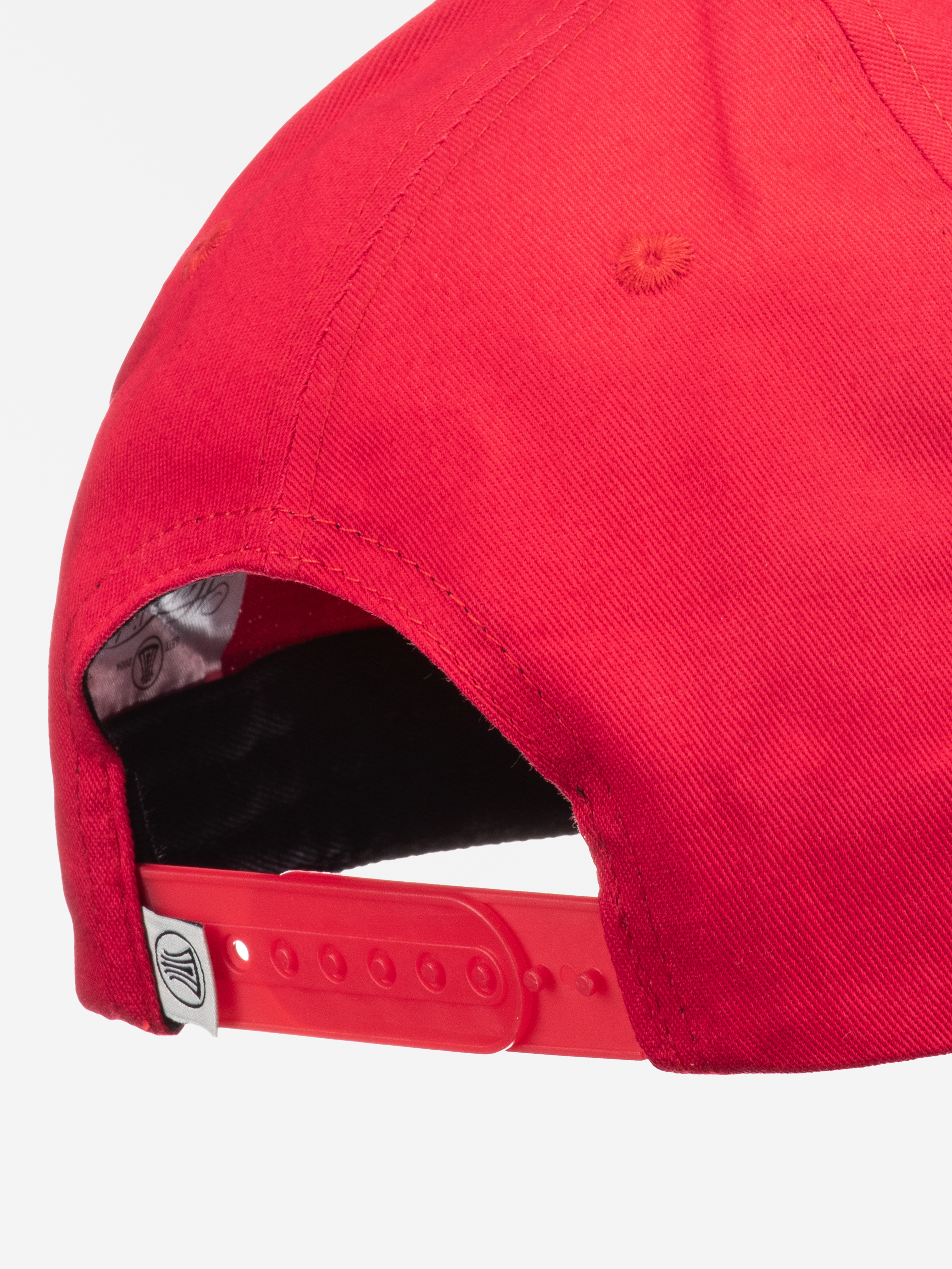 Nahaufnahme der Rückseite einer roten Baseballmütze mit einem verstellbaren Kunststoffband und einem kleinen weißen Anhänger mit schwarzem Logo. Die Nähte und Stoffdetails sind deutlich sichtbar.