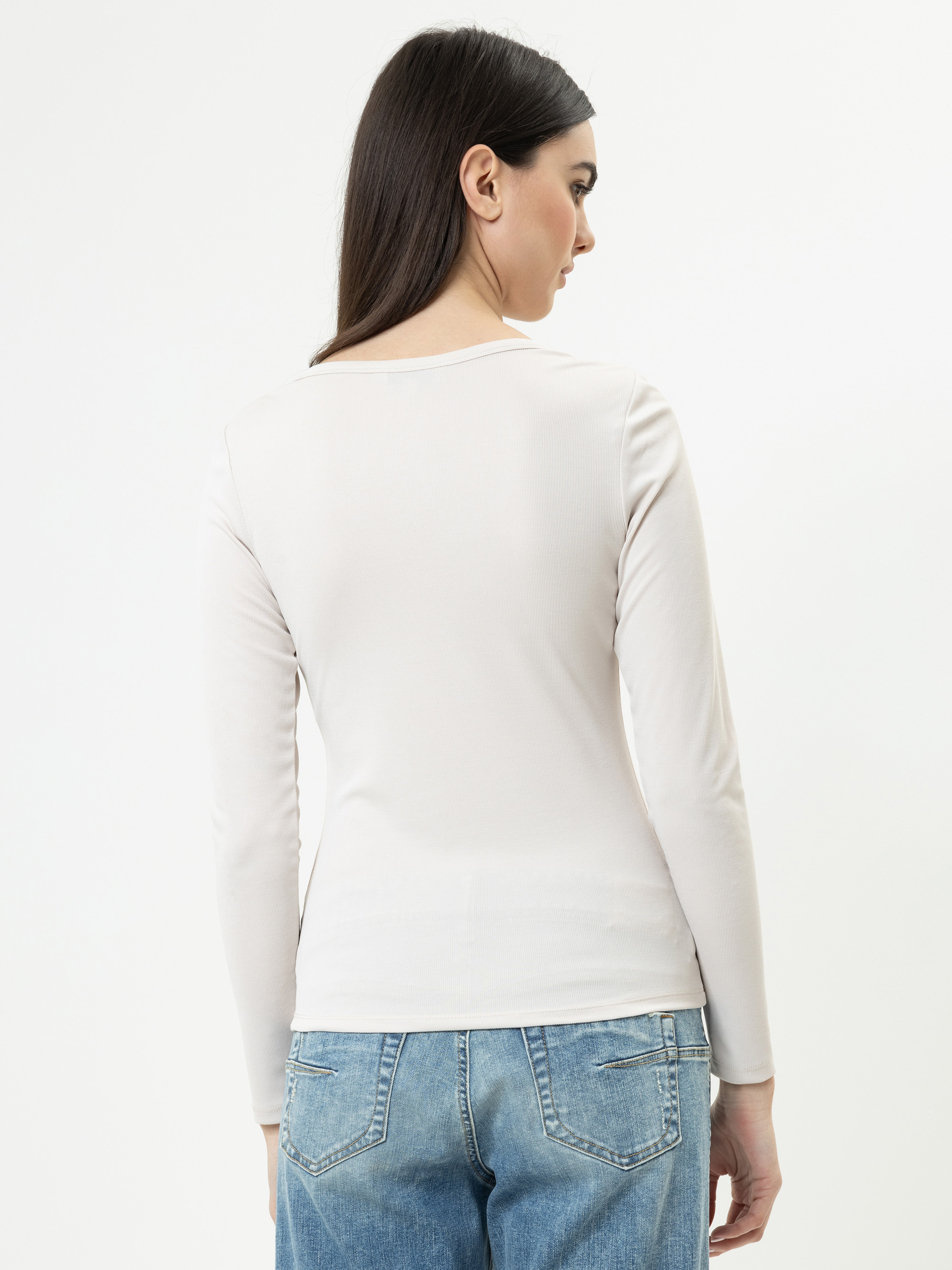 Eine Frau mit glattem dunklem Haar ist von hinten zu sehen. Sie trägt ein langärmeliges, helles Oberteil und blaue Jeans vor einem schlichten weißen Hintergrund.