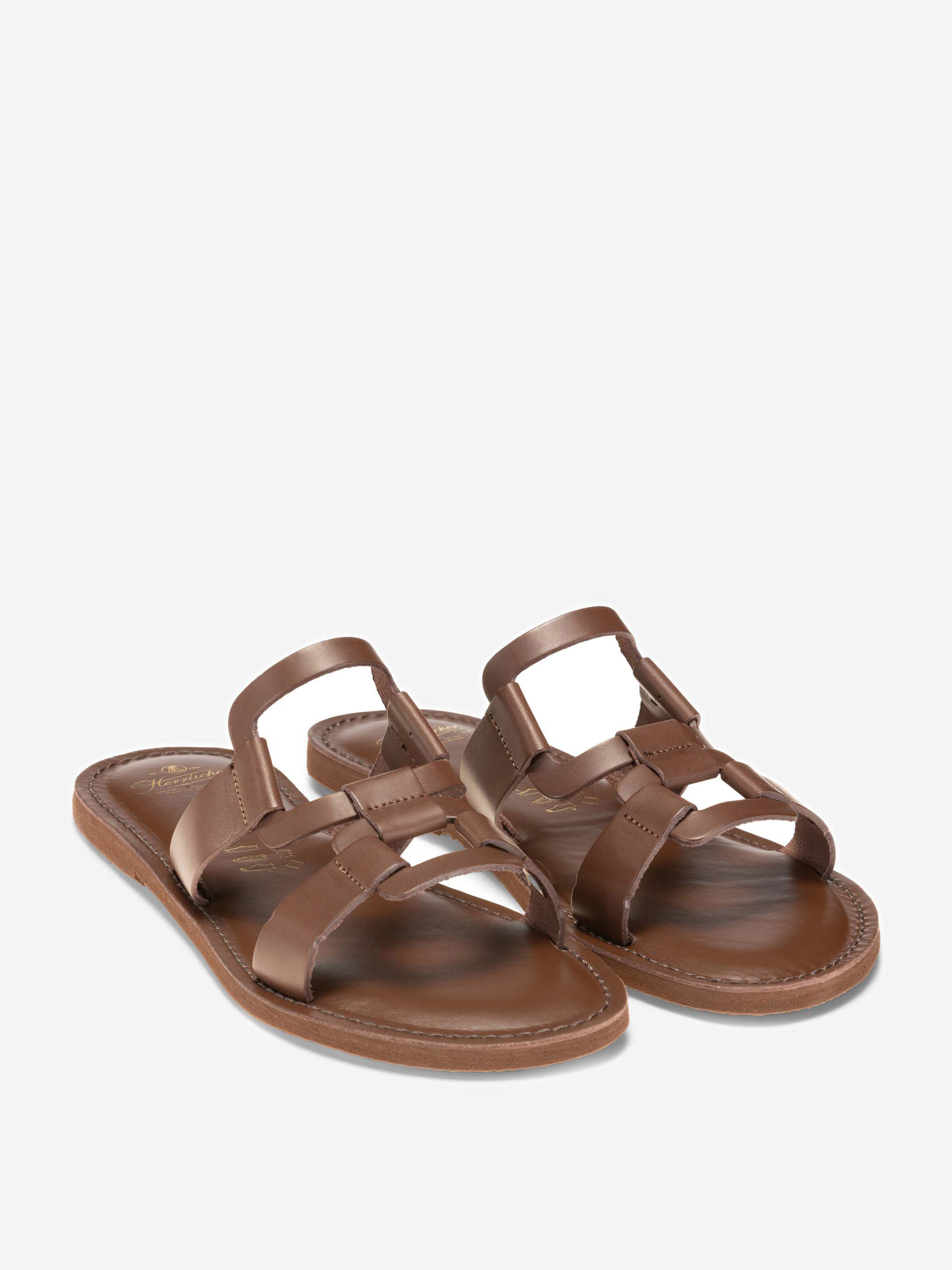 Flache Sandalen aus braunem Leder mit mehreren horizontalen und vertikalen Riemen, offener Spitze und einfachem Slip-on-Stil auf weißem Hintergrund.