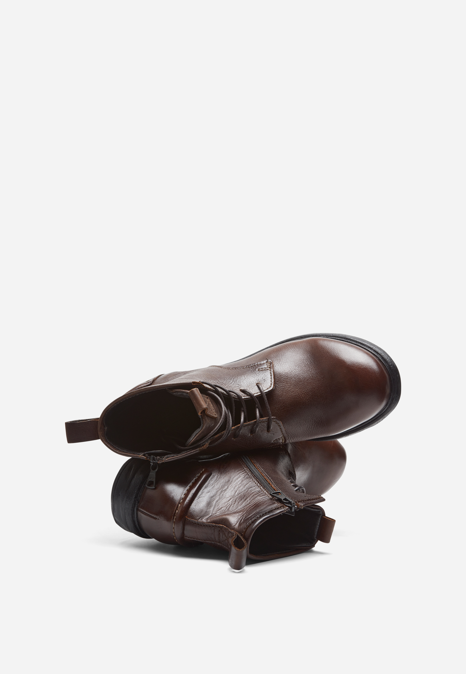 Ein Paar braune Lederstiefel mit seitlichen Reißverschlüssen und Zuglaschen, wobei ein Stiefel aufrecht steht und der andere dagegen gelehnt ist, dargestellt auf einem weißen Hintergrund.