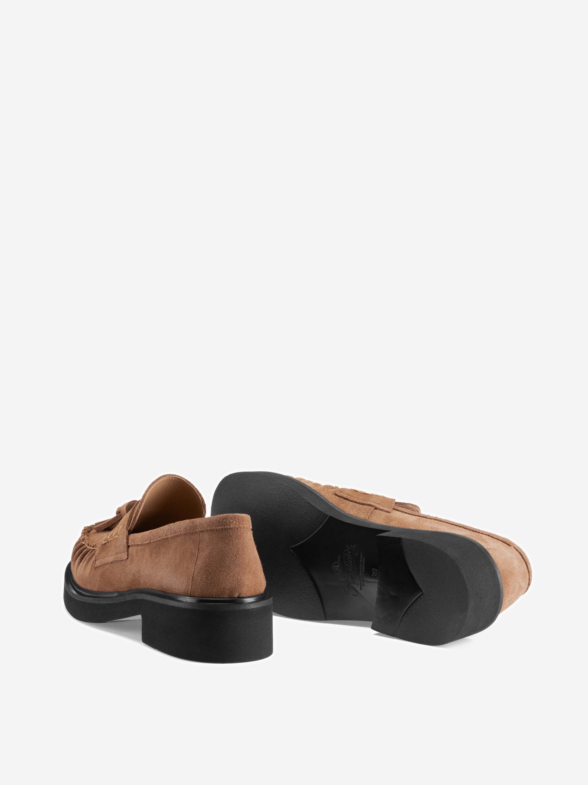 Ein Paar braune Wildleder-Loafer mit schwarzen Sohlen, wobei ein Schuh aufrecht steht und der andere auf der Seite liegt, sodass die Sohle und der Absatz vor einem schlichten weißen Hintergrund zu sehen sind.