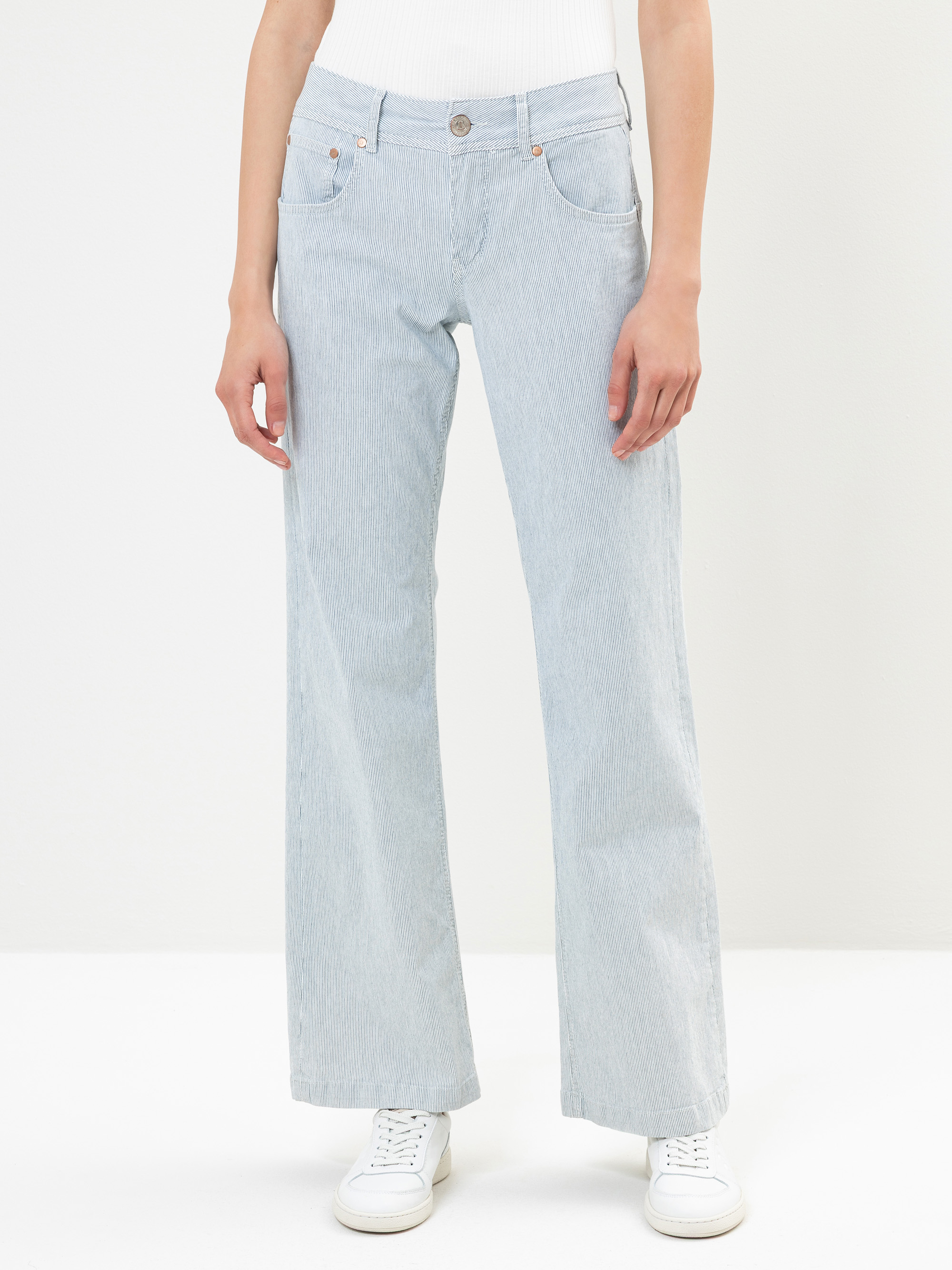 Eine Person in hellblauen, hoch taillierten, weit geschnittenen Jeans und weißen Turnschuhen steht vor einem schlichten weißen Hintergrund. Der Oberkörper ist größtenteils außerhalb des Bildausschnitts.