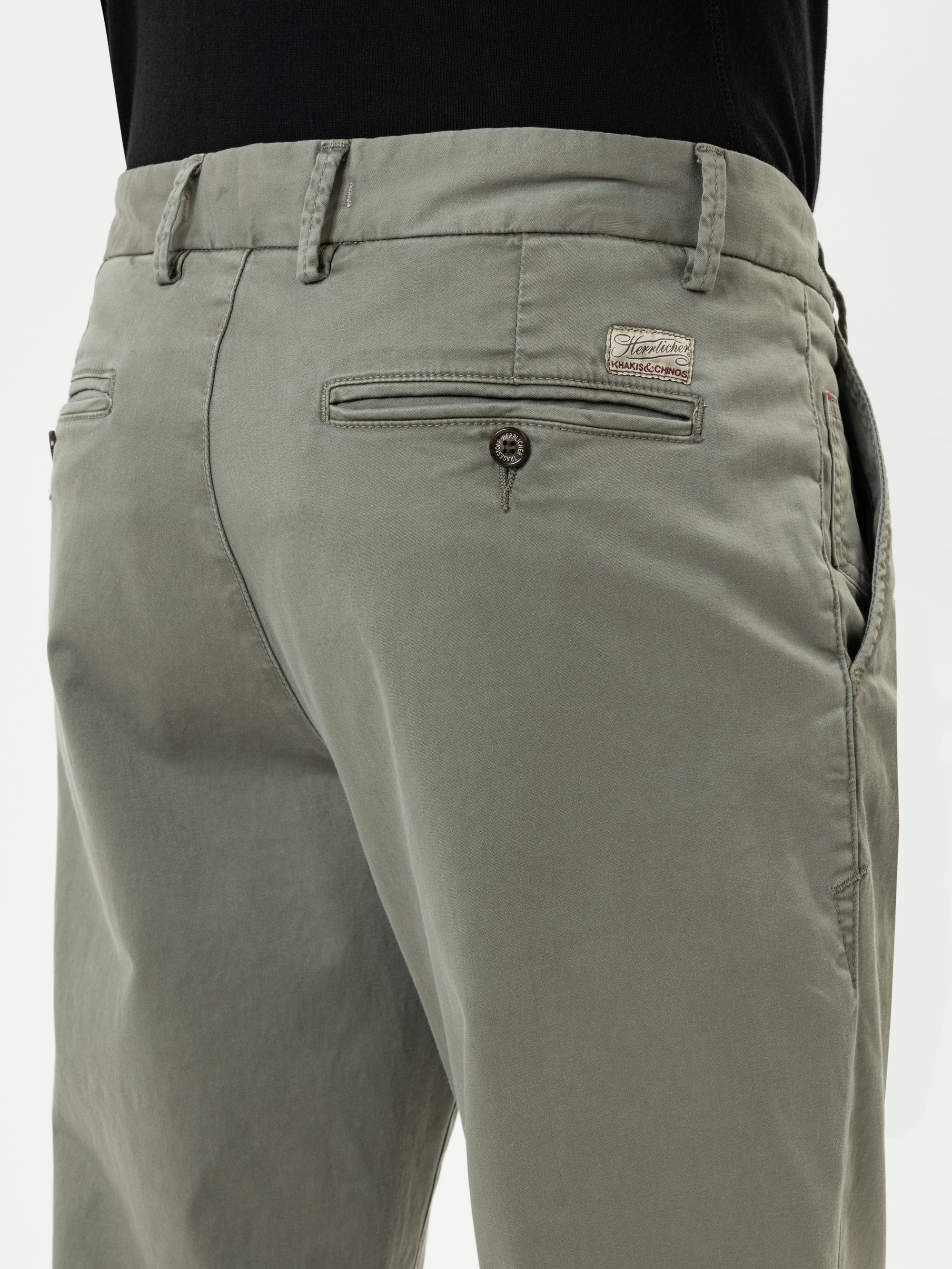 Eine Person, die eine hellgraue Hose mit Leistentaschen und einem Markenaufnäher über der rechten Gesäßtasche trägt, von der Taille abwärts und von hinten gesehen.