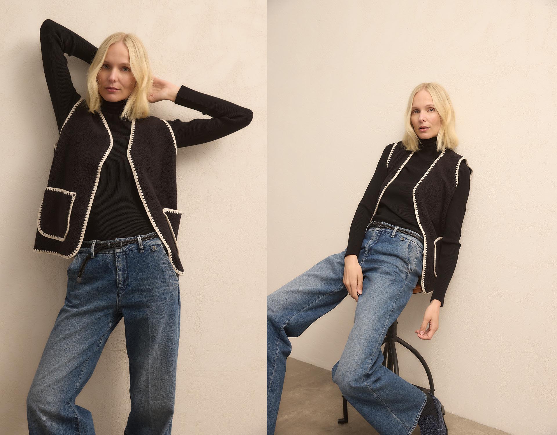 Zwei nebeneinander liegende Fotos einer blonden Frau in einem schwarzen langärmeligen Oberteil, einer schwarzen Strickweste mit weißem Saum und blauen Jeans, die vor einer schlichten hellen Wand posiert. Auf einer Aufnahme steht sie, auf der anderen sit