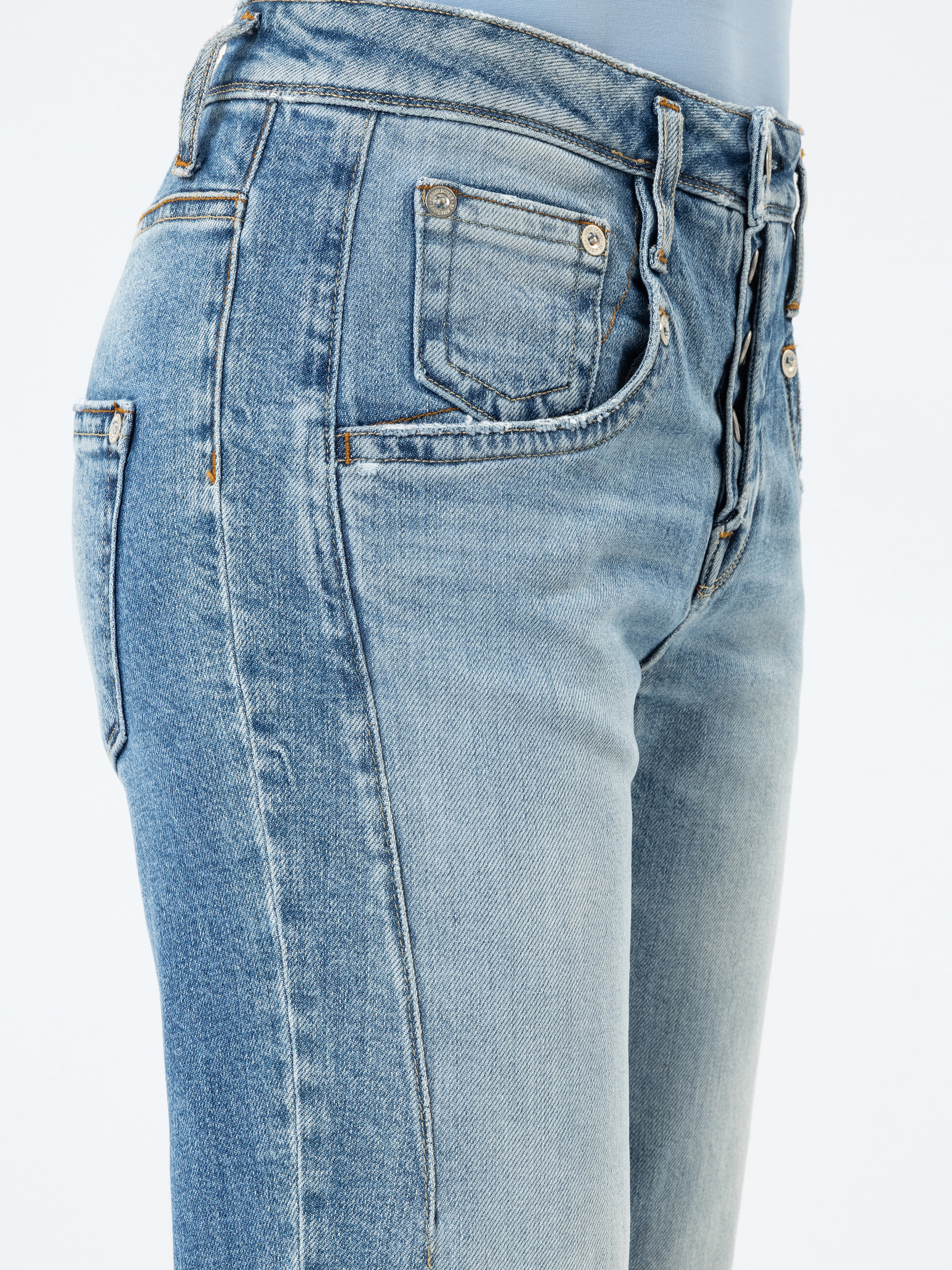 Nahaufnahme einer Person, die hellblaue, hoch taillierte, verblichene Jeans mit sichtbaren Nähten und Taschen vor einem einfarbigen Hintergrund trägt.