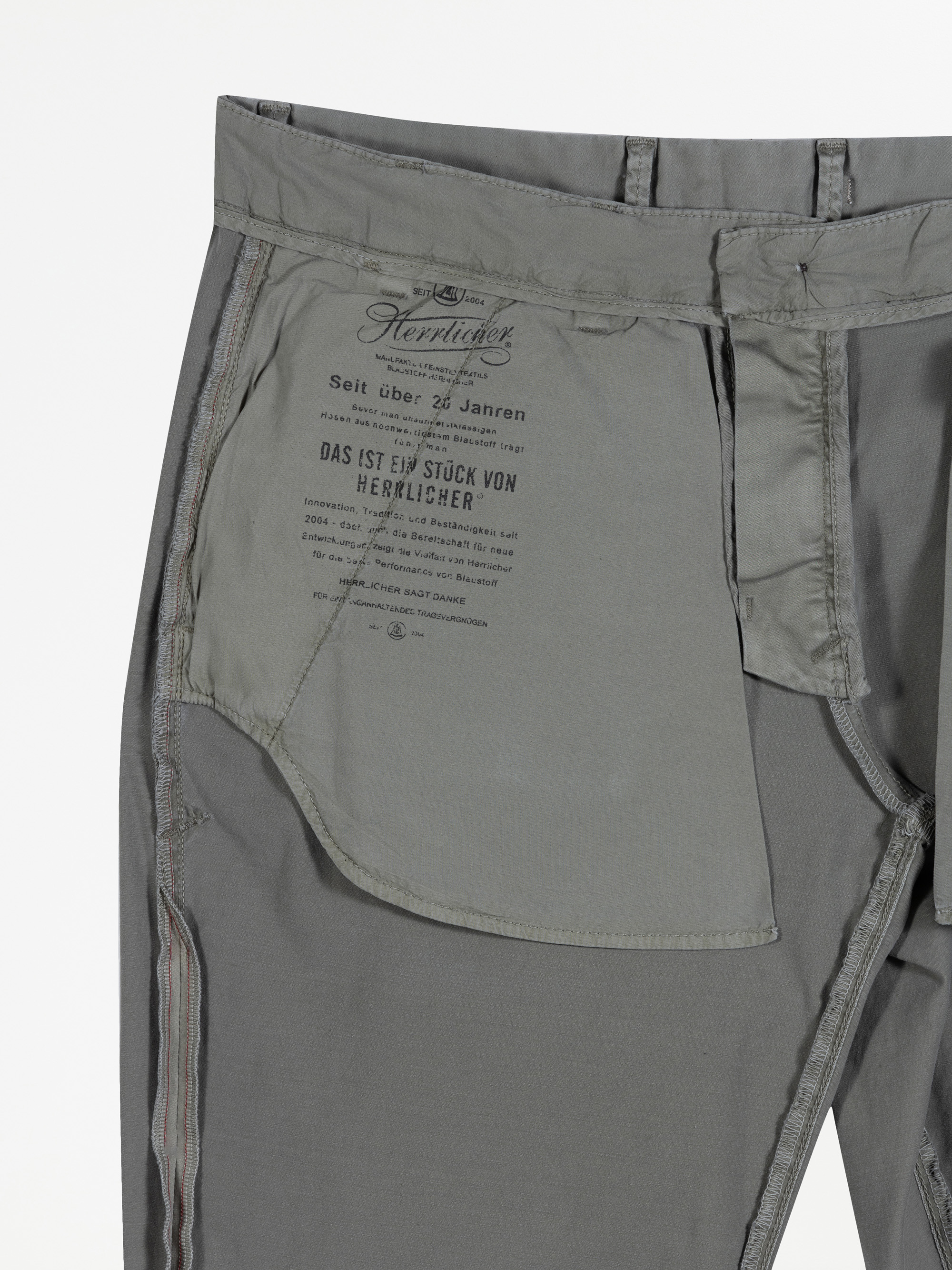 Nahaufnahme der Innenseite einer grauen Hose, die das Taschenfutter und den aufgedruckten Text mit Marken- und Pflegeinformationen in deutscher Sprache zeigt. Die Nähte sind deutlich sichtbar.