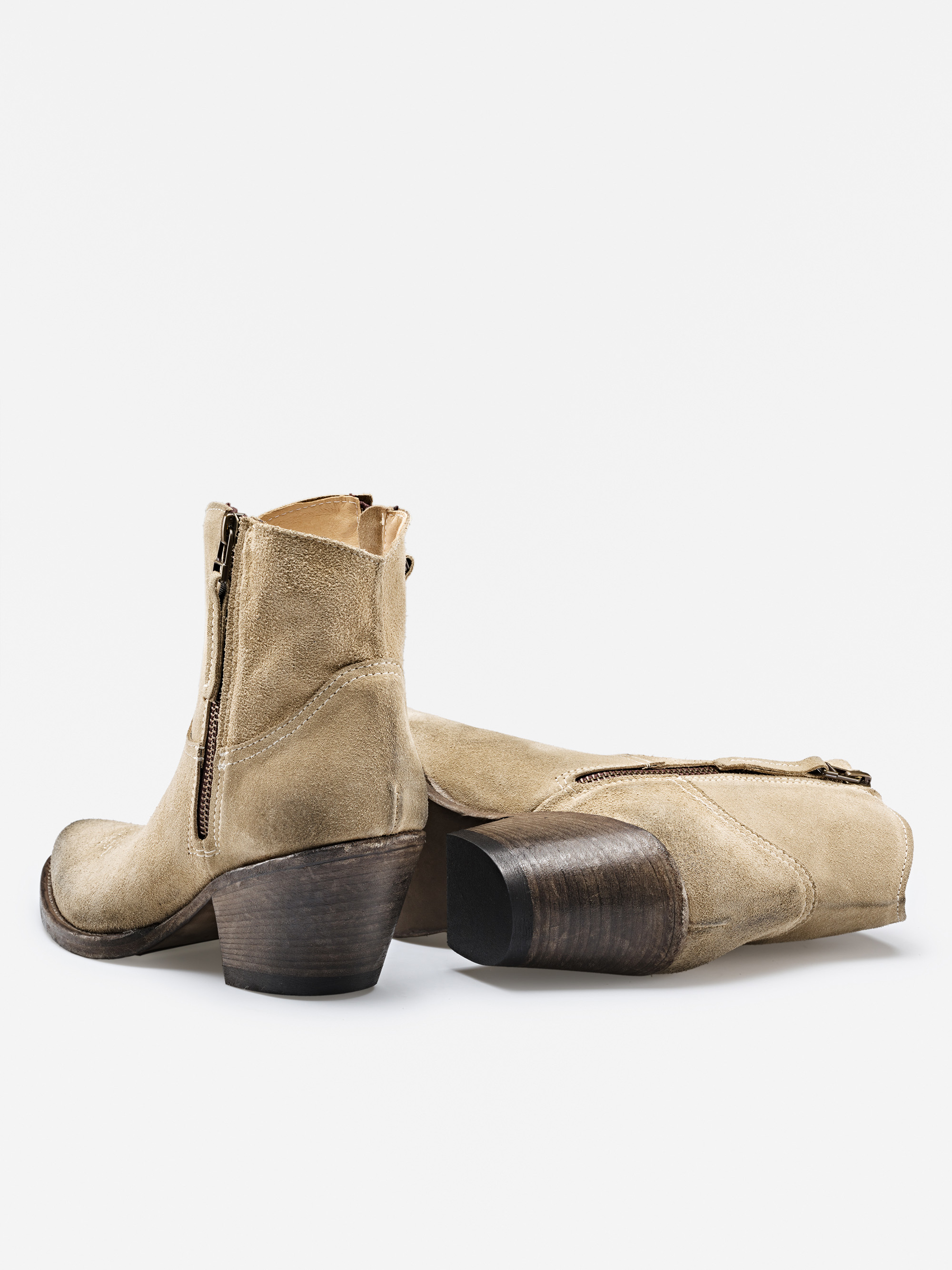 Ein Paar hellbraune Wildlederstiefel mit seitlichen Reißverschlüssen und gestapelten Holzabsätzen, wobei ein Stiefel aufrecht steht und der andere auf der Seite liegt, dargestellt auf einem weißen Hintergrund.