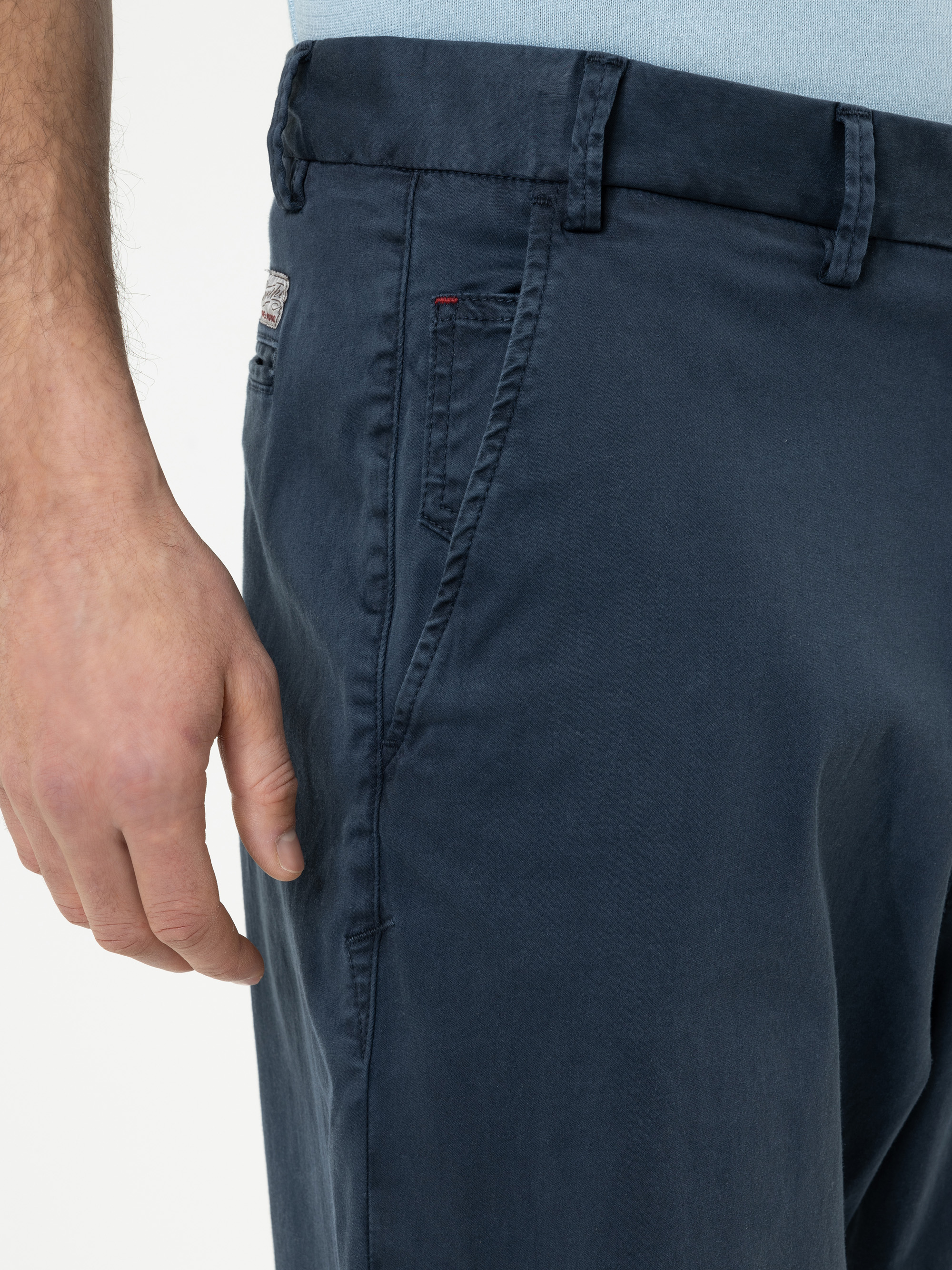 Nahaufnahme einer Person, die eine marineblaue Hose und ein hellblaues Hemd trägt, wobei die linke Hand in der Nähe der Vordertasche ruht. Nur der untere Teil des Oberkörpers und ein Teil des Arms sind sichtbar.