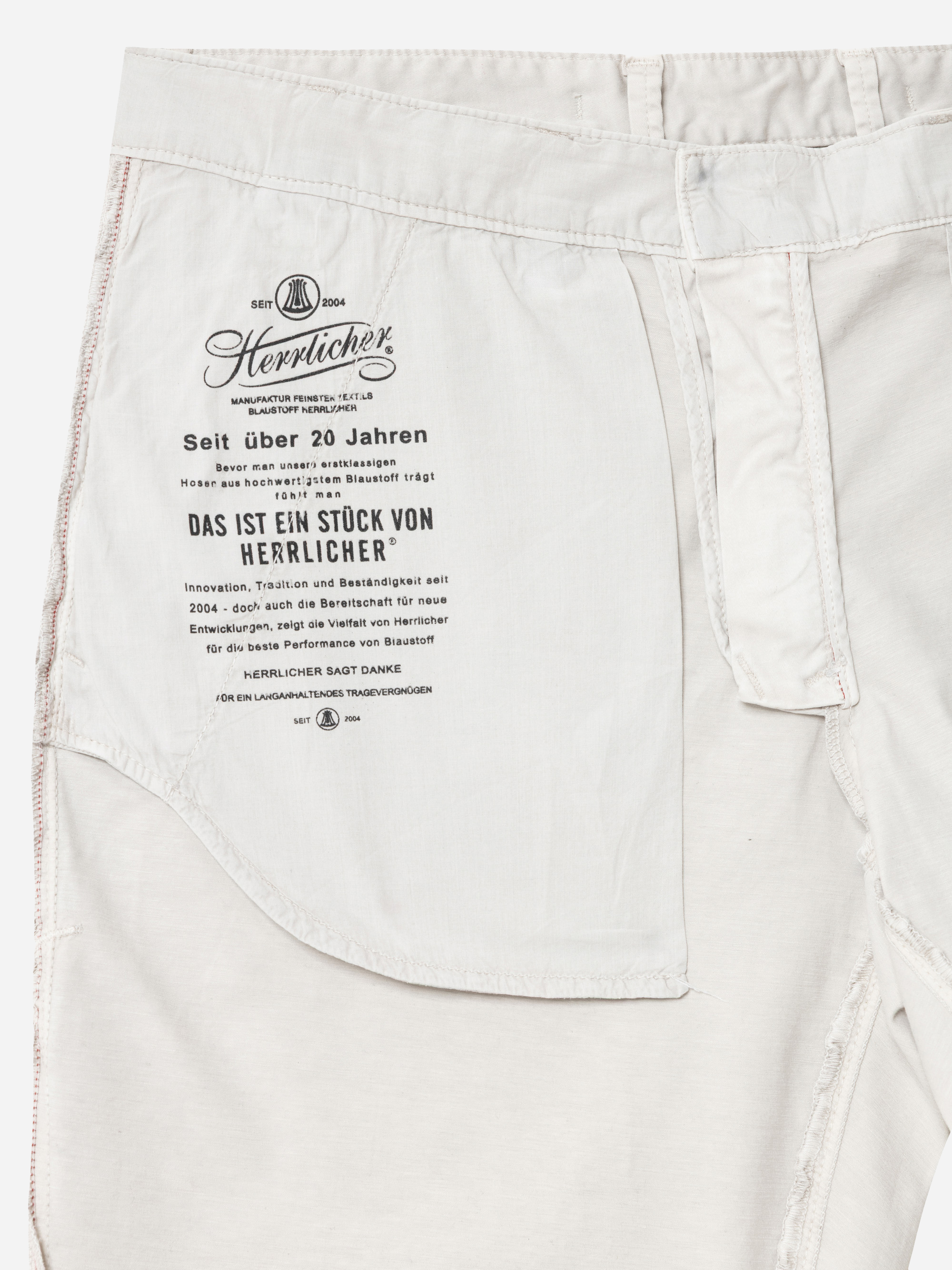 Nahaufnahme der Innenseite einer hellen Hose mit aufgedrucktem Text in deutscher Sprache auf dem Taschenfutter, mit sichtbaren Nähten und Stoffdetails.