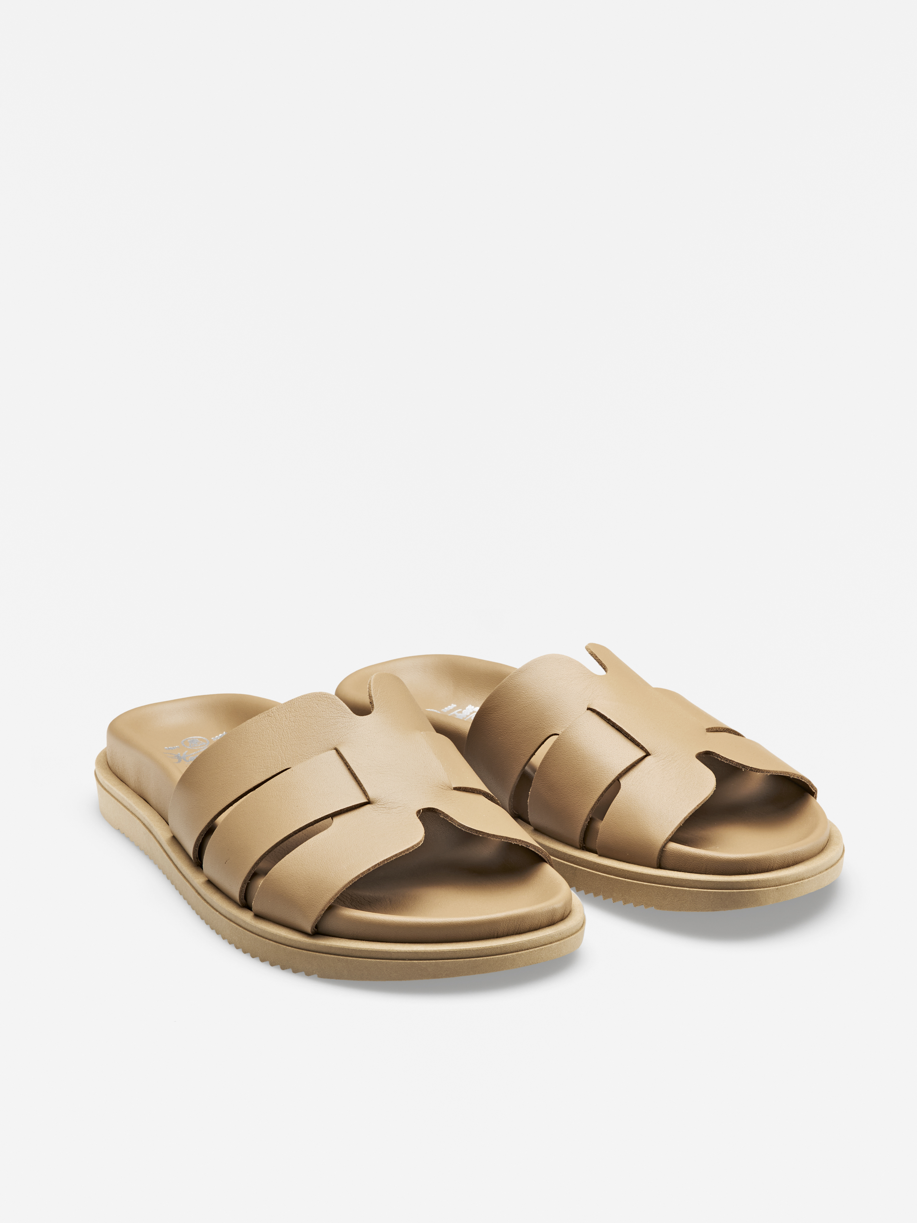 Ein Paar beigefarbene Gleitsandalen mit breiten, ineinandergreifenden Lederriemen und flachen Sohlen, dargestellt auf weißem Hintergrund.