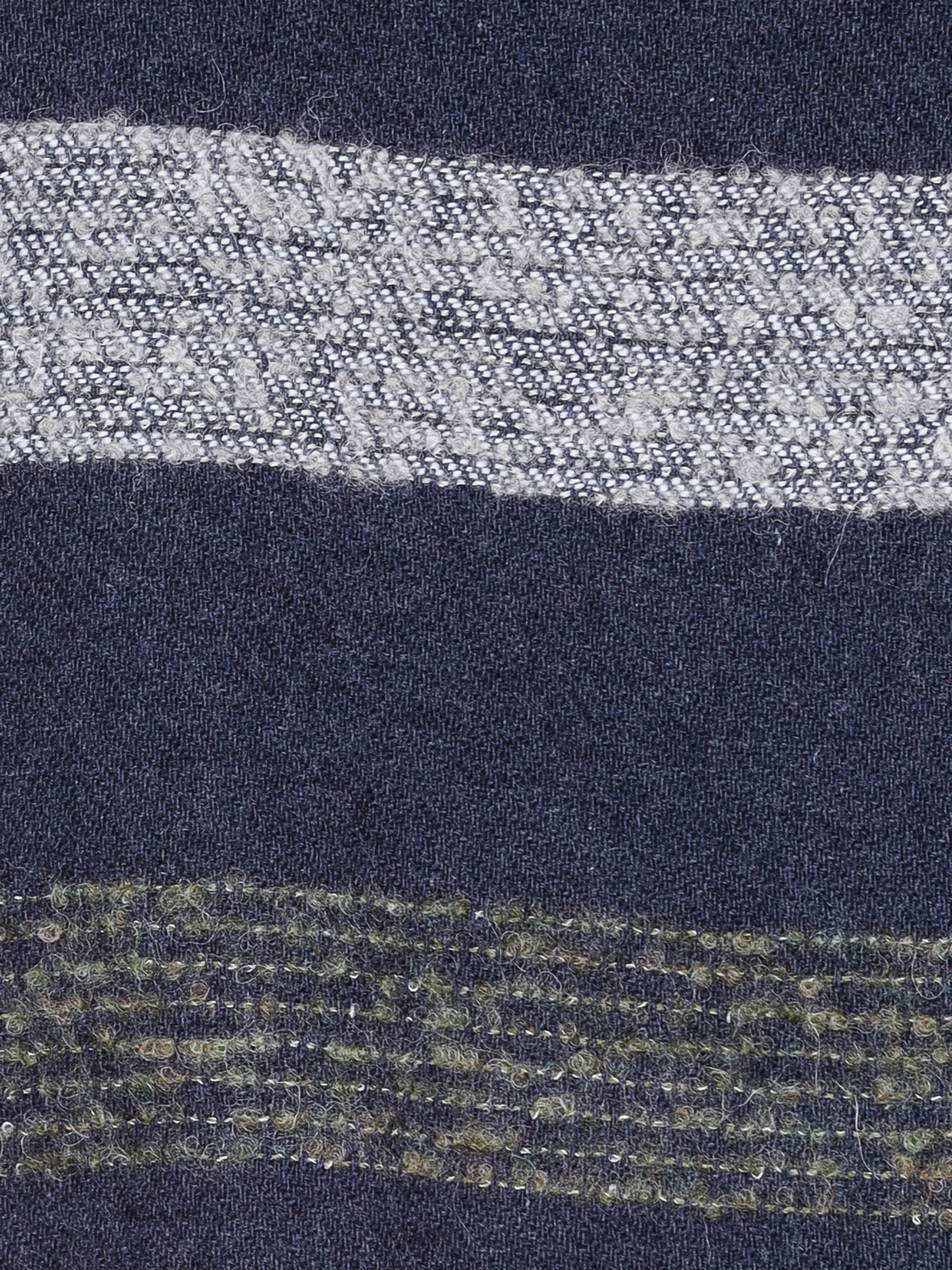 Nahaufnahme eines Stoffes mit dunkelblauem Hintergrund, der im oberen Bereich einen breiten, strukturierten weißen Streifen und im unteren Bereich einen schmaleren, strukturierten grünlichen Streifen aufweist. Die Streifen haben ein gewebtes Aussehen.