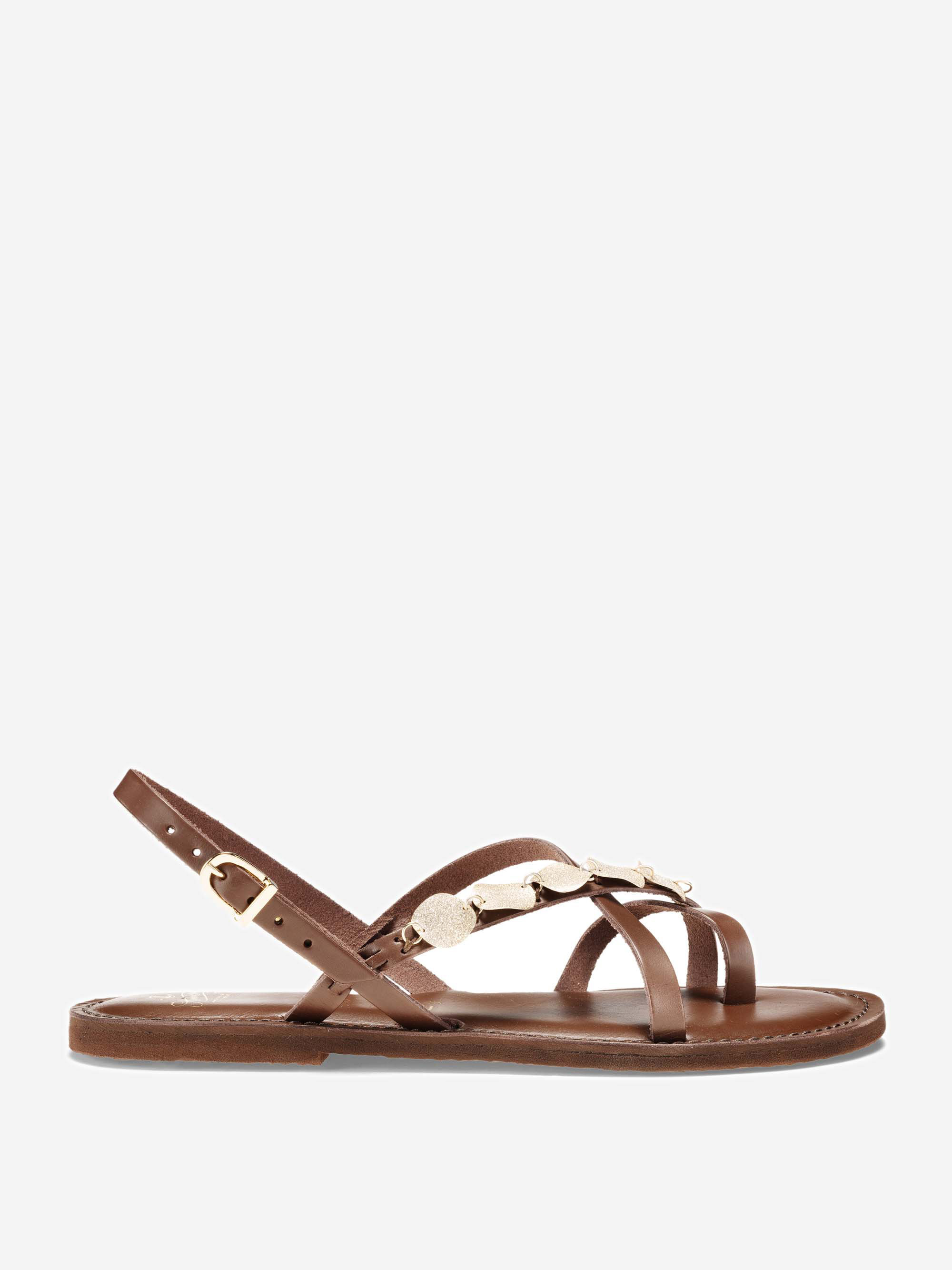 Eine braune, flache Sandale mit dünnen Lederriemen, einer seitlichen Schnalle und dekorativen, goldfarbenen Metallakzenten auf der Oberseite. Die Sandale ist auf einem weißen Hintergrund abgebildet.