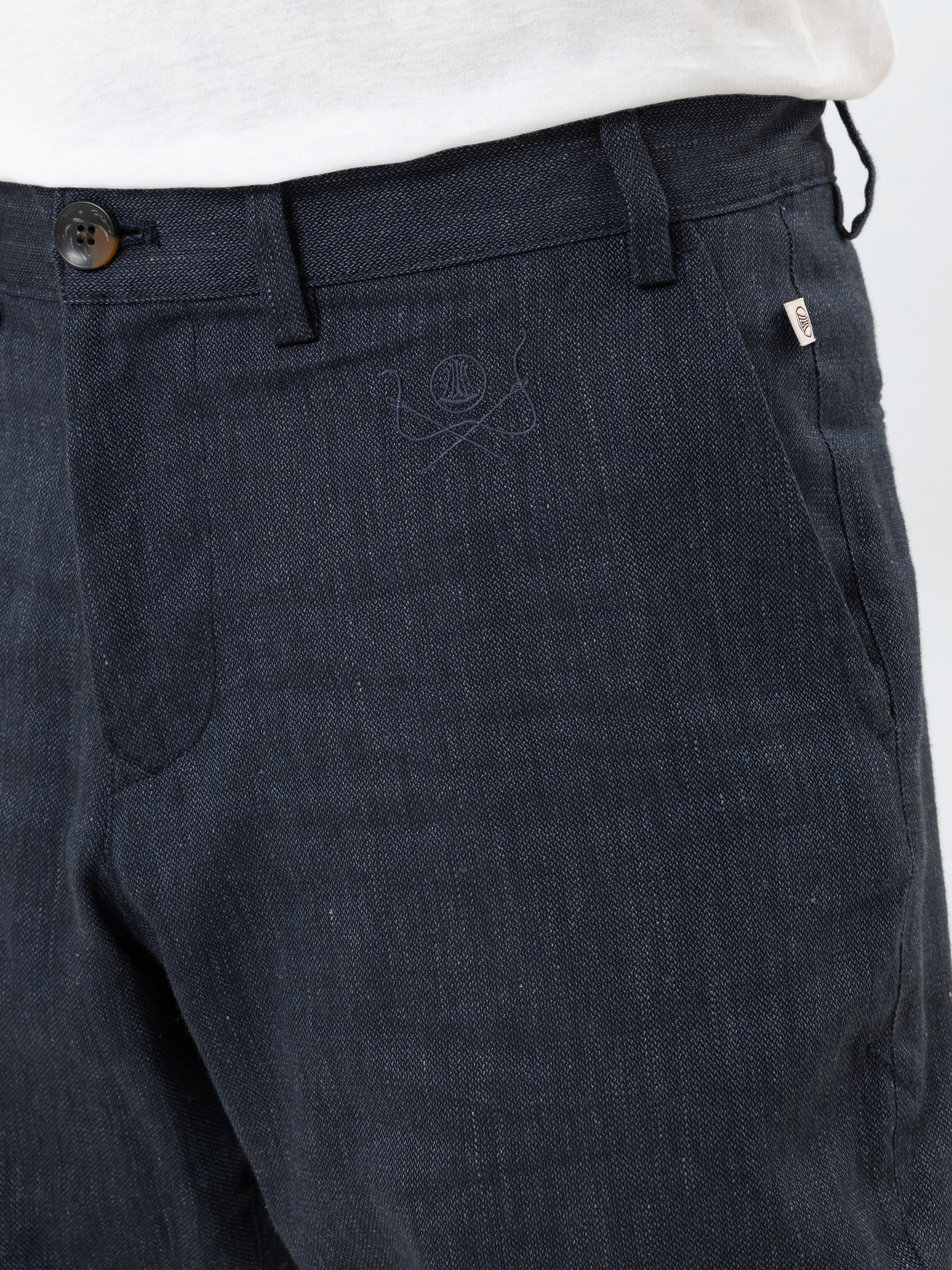 Nahaufnahme einer Person, die eine dunkelblaue Jeanshose mit einem sichtbaren Knopf, Gürtelschlaufen und einer Vordertasche trägt; an der Taille ist ein Teil eines weißen Hemdes zu sehen.