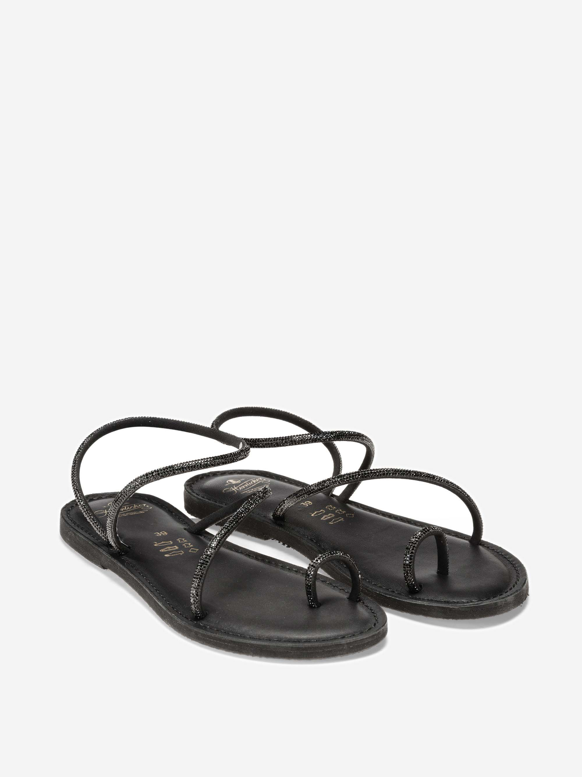 Ein Paar schwarzer flacher Riemchensandalen mit dünnen, minimalistischen Riemen, die sich über die Spitze und die Zehen kreuzen, auf weißem Hintergrund.