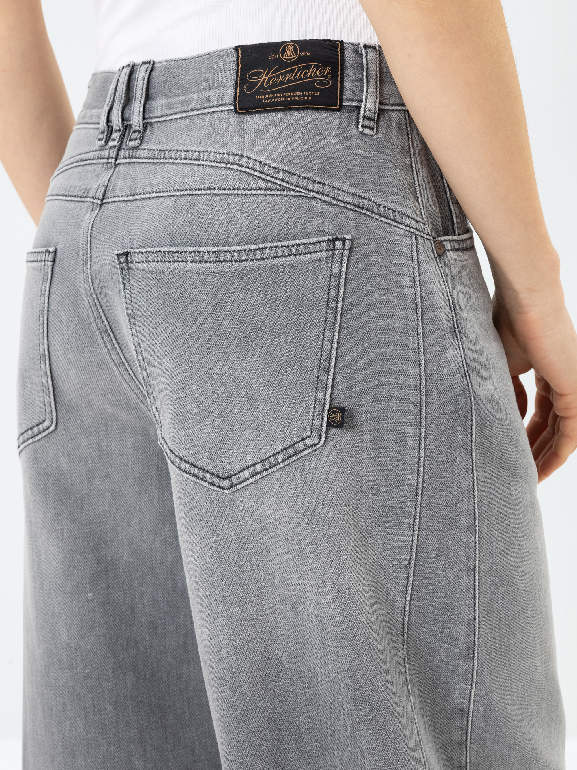 Eine Person, die eine hellgraue Jeans mit hoher Taille trägt, von hinten gesehen, wobei die Gesäßtaschen und ein schwarzes Markenetikett am Bund zu sehen sind.