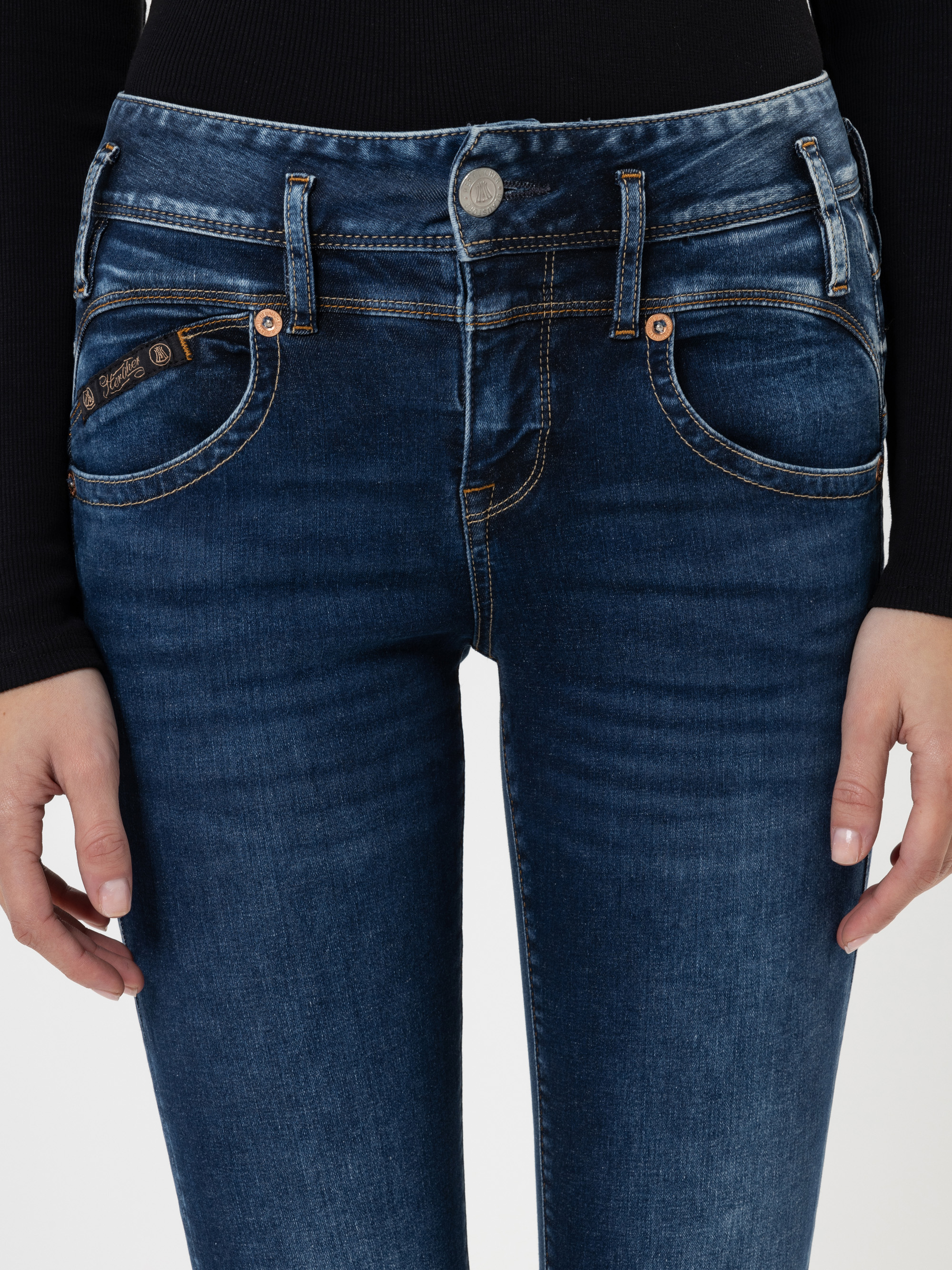 Eine Person, die eine dunkelblaue Jeans und ein schwarzes langärmeliges Oberteil trägt, von der Taille bis zu den Oberschenkeln, die Hände locker an der Seite.