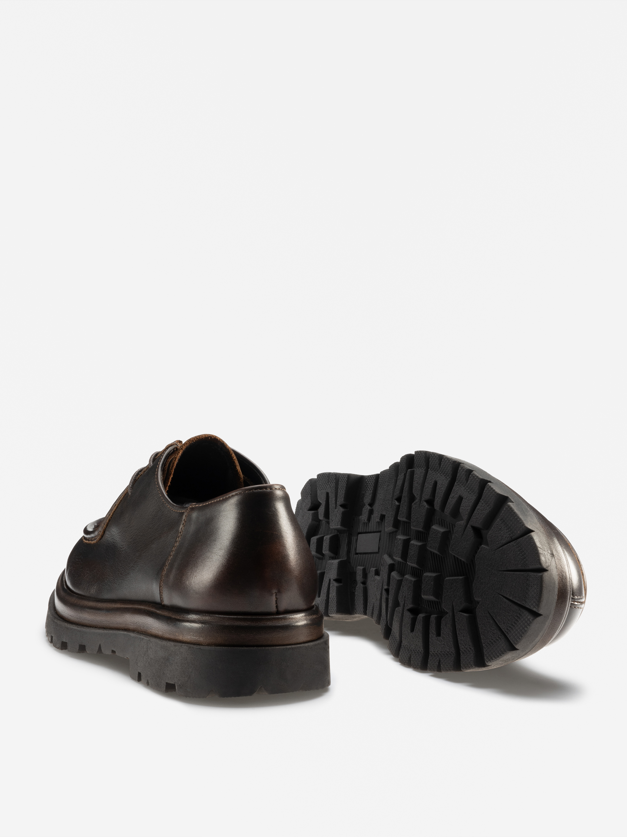 Ein Paar dunkelbraune Lederschnürschuhe, dargestellt vor einem weißen Hintergrund. Ein Schuh steht aufrecht, der andere ist so positioniert, dass seine schwarze, raue, strukturierte Sohle sichtbar ist.