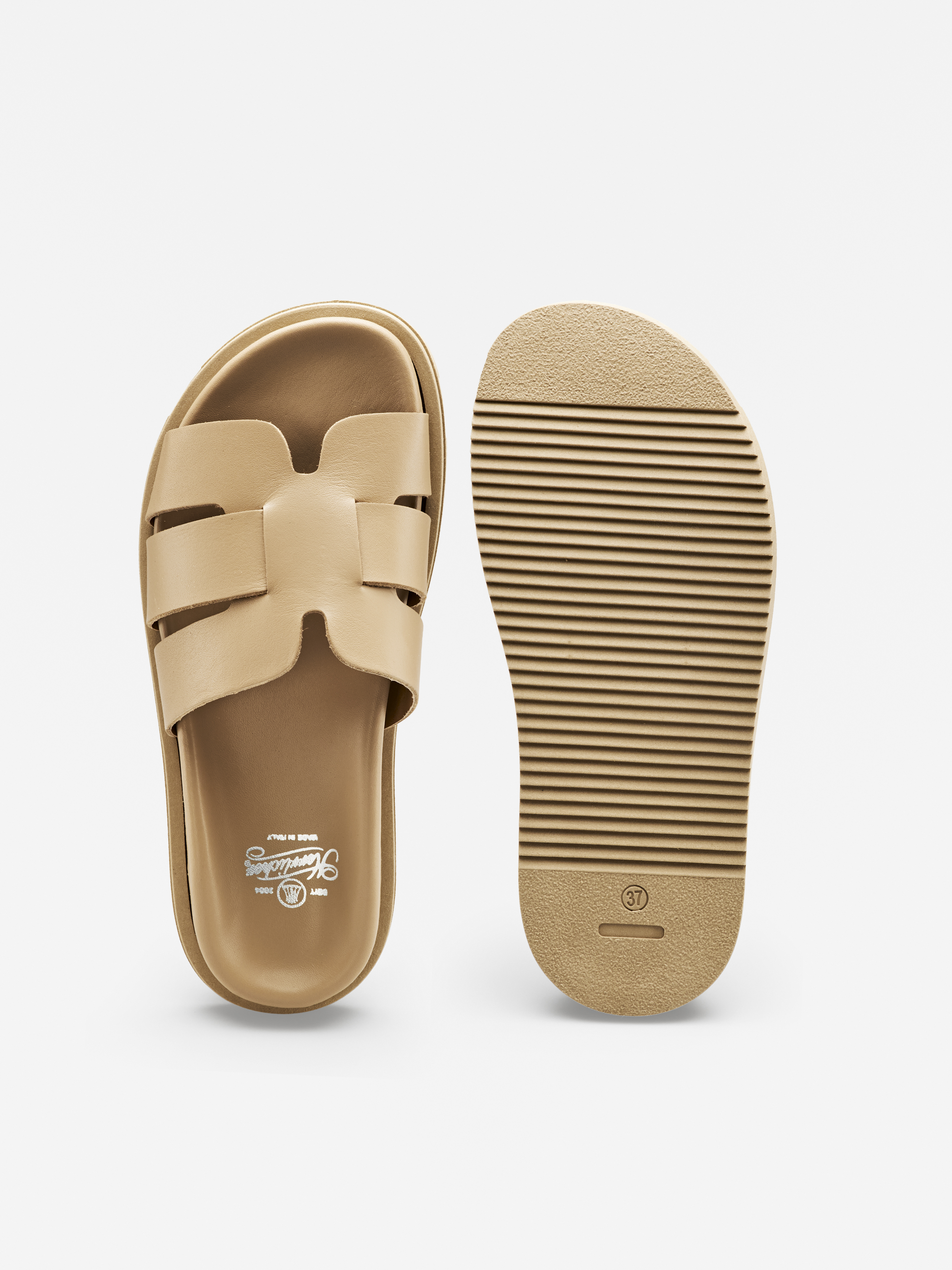 Abgebildet ist ein Paar beigefarbener Slipper; eine Sandale zeigt das Oberteil mit breiten, sich kreuzenden Riemen, die andere die Sohle mit horizontalen Rillen für den Halt, beide vor weißem Hintergrund.