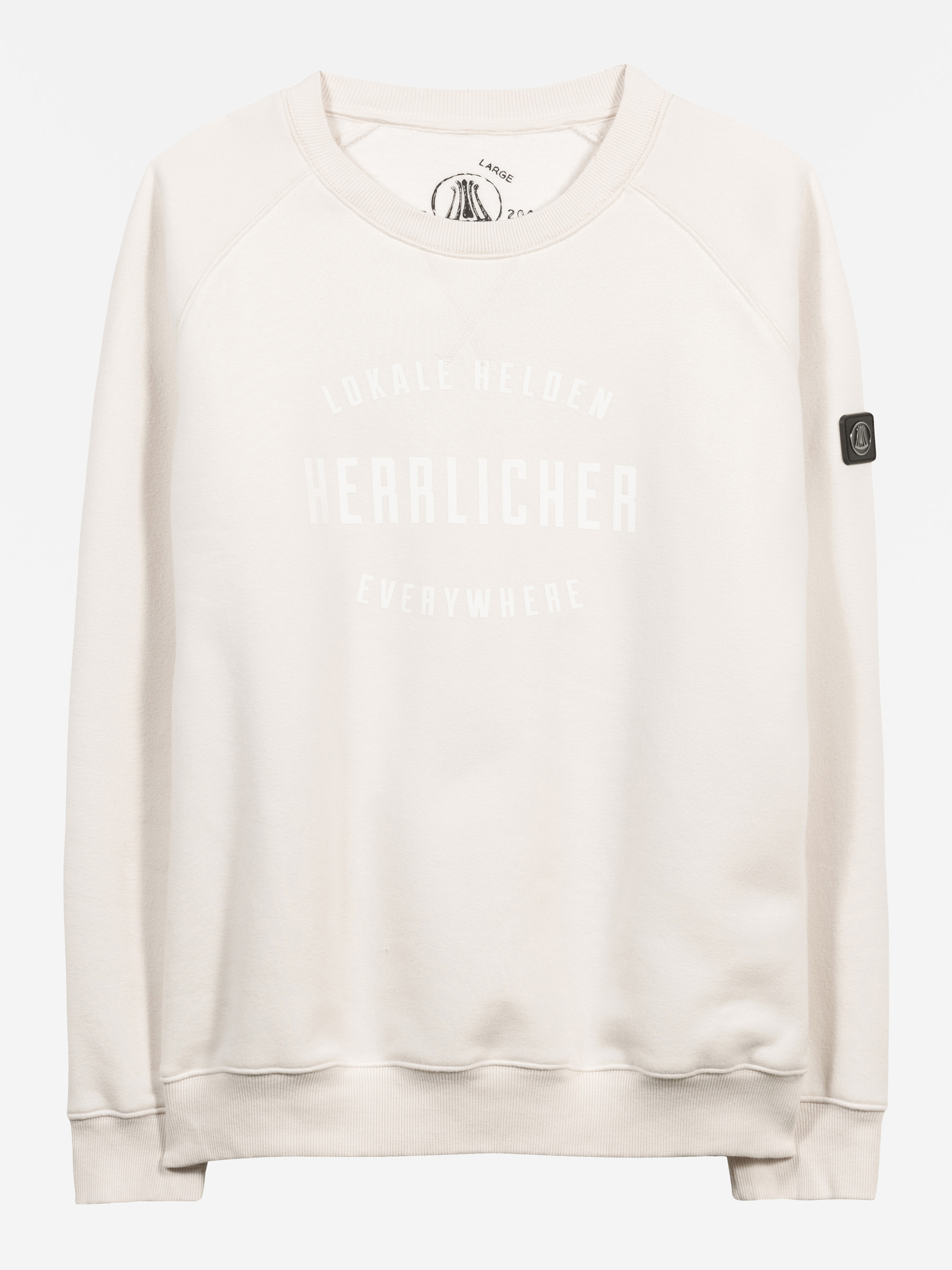 Ein hellbeiges Sweatshirt mit dem Aufdruck LOKALE HELDEN HERZLICHER EVERYWHERE in weißer Schrift auf der Vorderseite und einem kleinen schwarzen Patch auf dem linken Ärmel. Das Sweatshirt hat einen Rundhalsausschnitt und gerippte Bündchen und Saum.