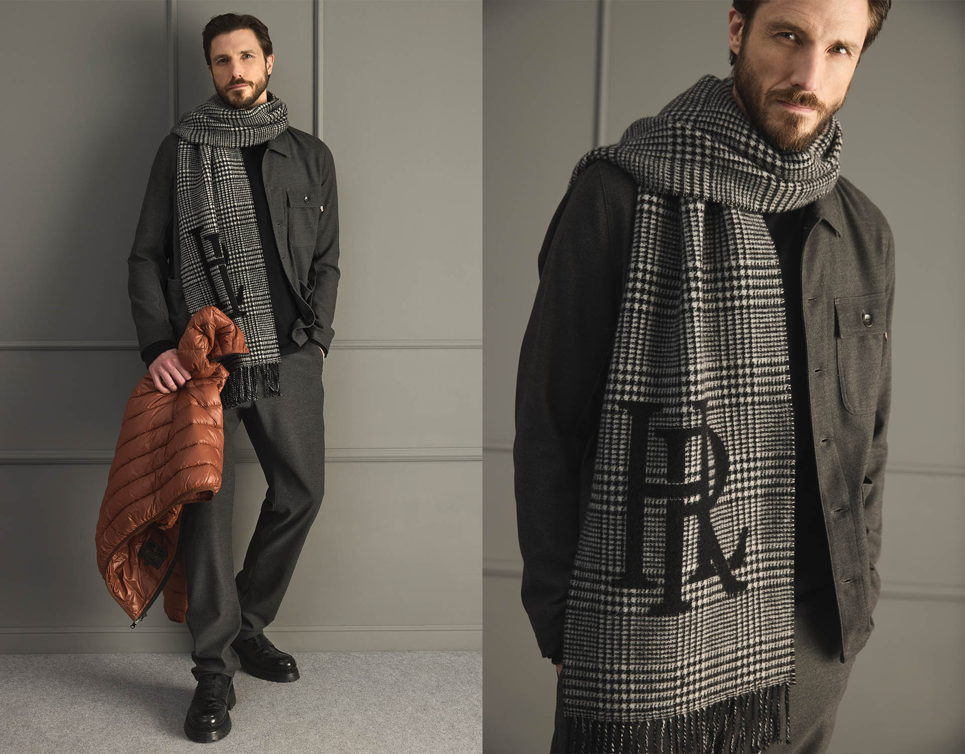 Ein Mann, der ein schwarzes Hemd, eine graue Hose und schwarze Schuhe trägt, steht in einem Haus und hält eine braune Steppjacke. Um seinen Hals hat er einen großen schwarz-weiß karierten Schal mit den Initialen LR drapiert.