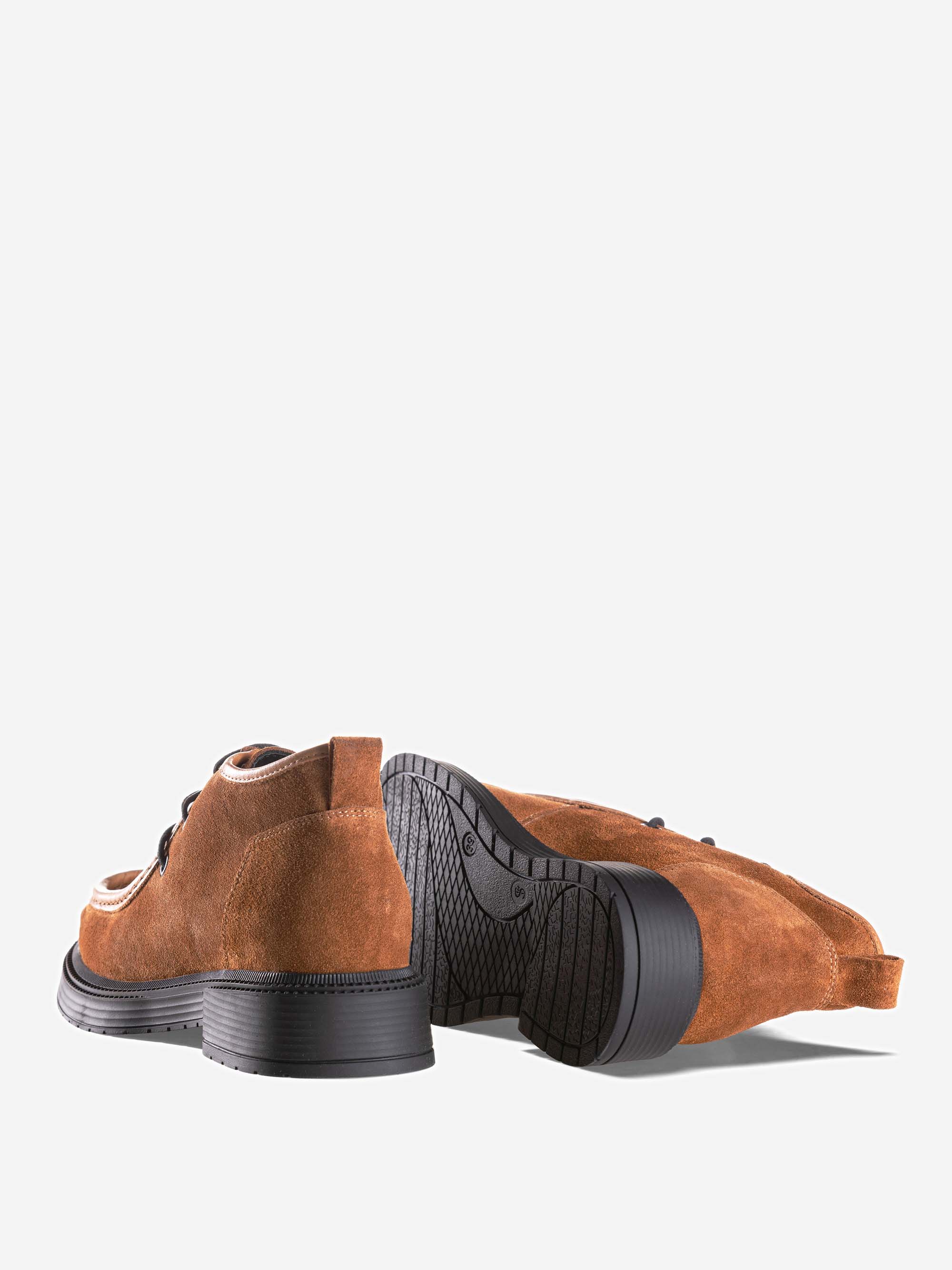 Ein Paar braune Wildleder-Schnürschuhe mit schwarzen Gummisohlen, wobei ein Schuh aufrecht steht und der andere auf der Seite liegt, sodass das Profil der Sohle sichtbar ist, vor einem schlichten weißen Hintergrund.