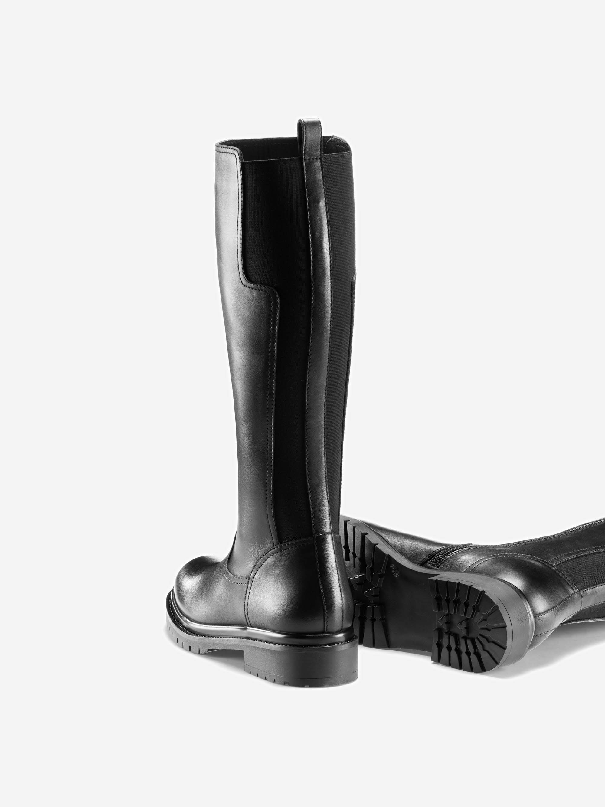 Ein Paar hohe schwarze Lederstiefel mit klobigen Sohlen; ein Stiefel steht aufrecht, während der andere auf der Seite liegt, sodass man das Profil an der Unterseite sehen kann.