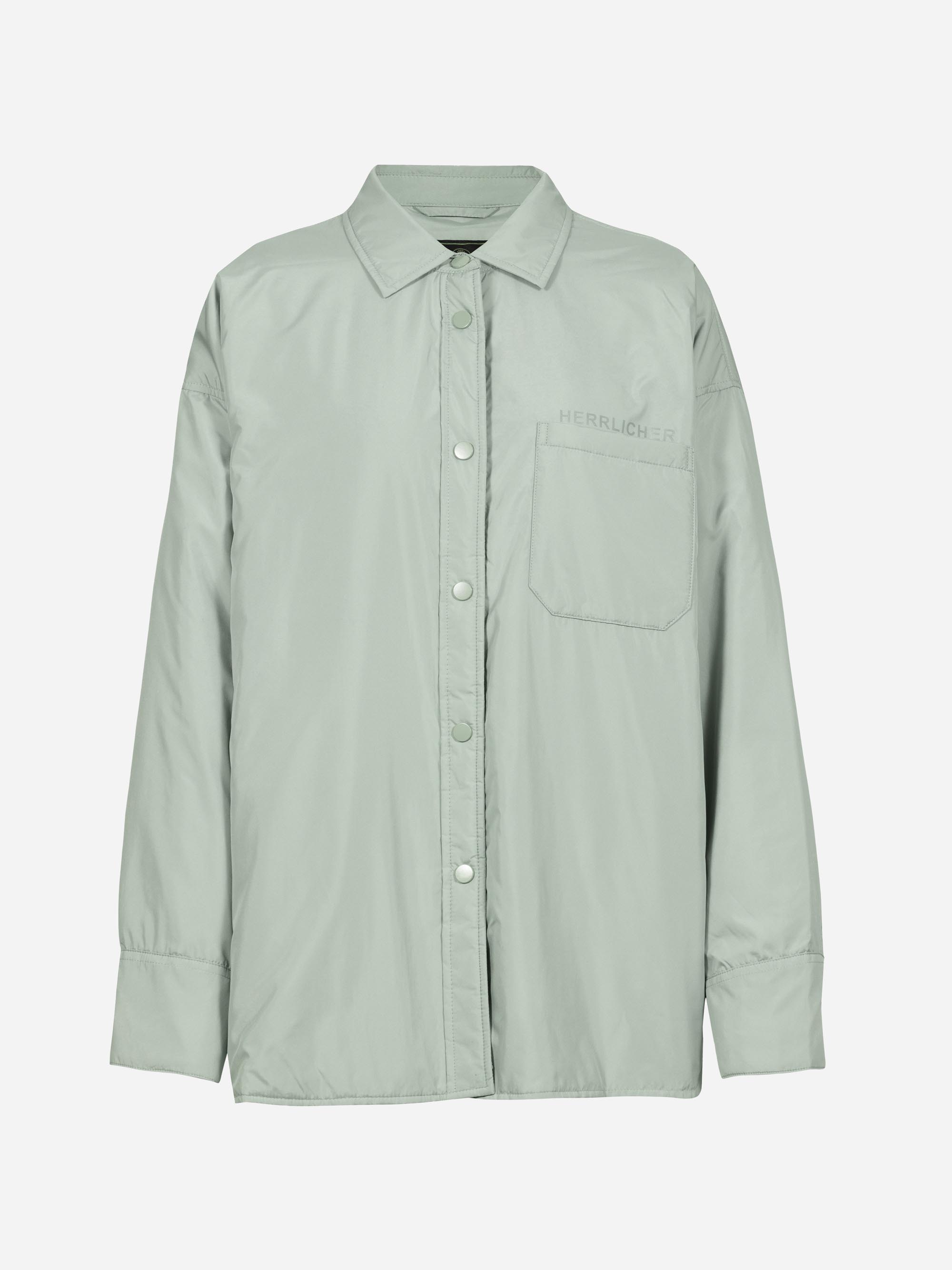 Helles salbeigrünes Hemd mit langen Ärmeln, spitzem Kragen, Druckknöpfen vorne und einer einzelnen Brusttasche auf der linken Seite. Der Stoff ist glatt und leicht glänzend, über der Tasche ist das Wort Herrlicher aufgestickt.