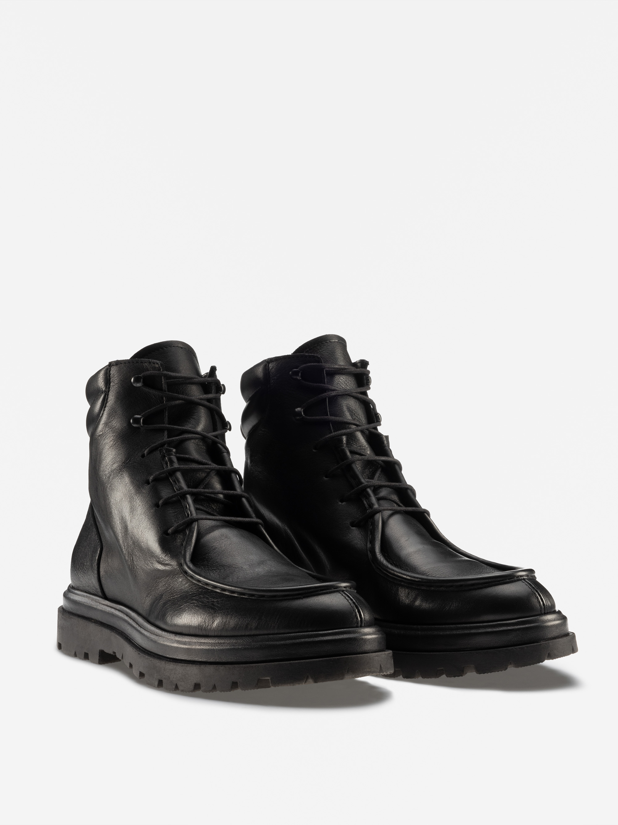 Ein Paar schwarze Lederstiefel zum Schnüren mit dicken, robusten Sohlen, die vor einem schlichten weißen Hintergrund gezeigt werden. Die Stiefel haben eine polierte Oberfläche und ein robustes, strukturiertes Design.