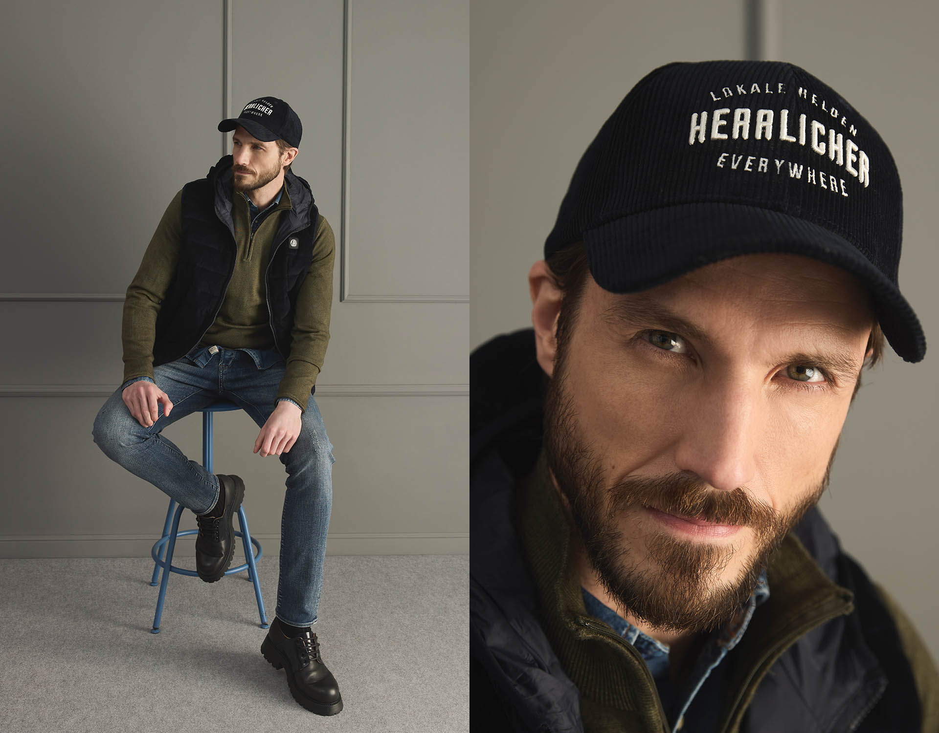 Ein Mann mit Bart trägt eine schwarze Mütze, eine dunkle Weste, einen olivgrünen Pullover, Jeans und schwarze Stiefel und sitzt auf einem Hocker in einem modernen Raum. Eine Nahaufnahme zeigt den Text der Mütze: "HERALICHER EVERYWHERE.".