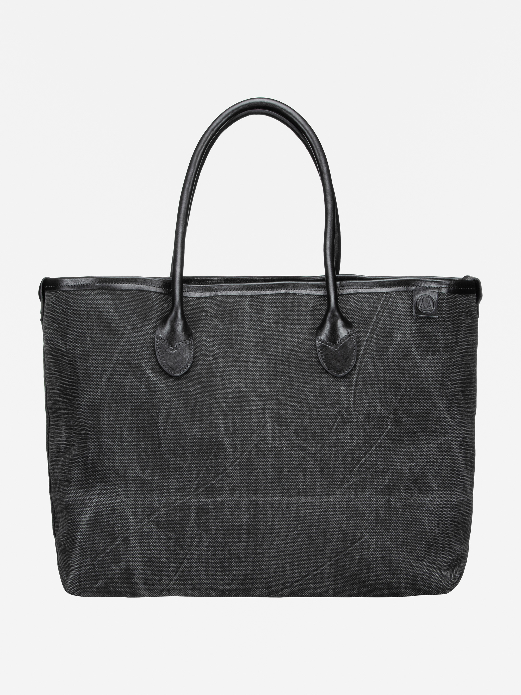 Eine große schwarze Tragetasche mit zwei Henkeln aus strukturiertem Stoff und mit Lederakzenten an den Henkeln und am oberen Rand vor einem schlichten weißen Hintergrund.