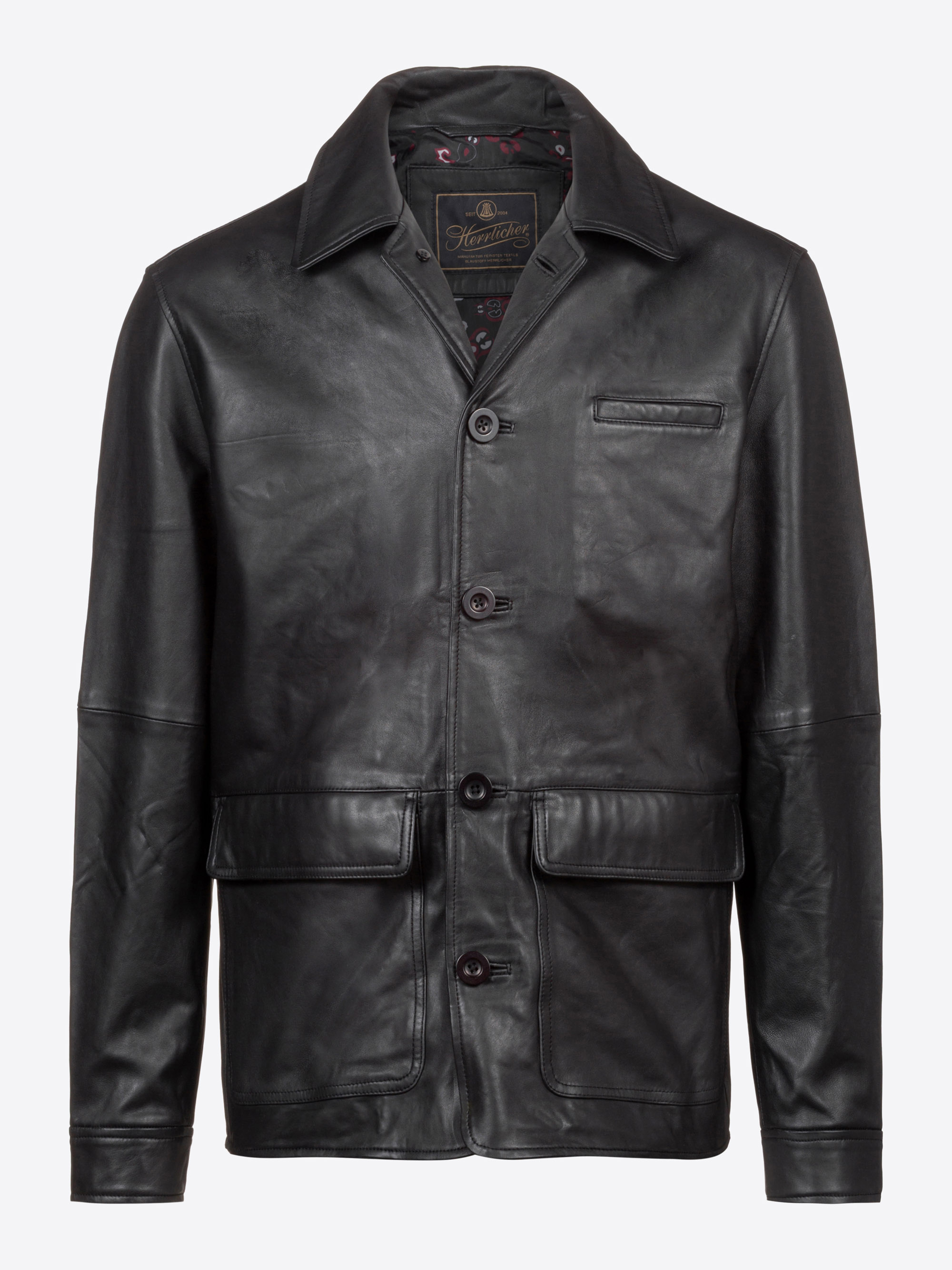 Schwarze Lederjacke mit geknöpfter Vorderseite, gekerbtem Kragen, einer Brusttasche und zwei großen Pattentaschen auf der Vorderseite vor einem schlichten hellen Hintergrund.